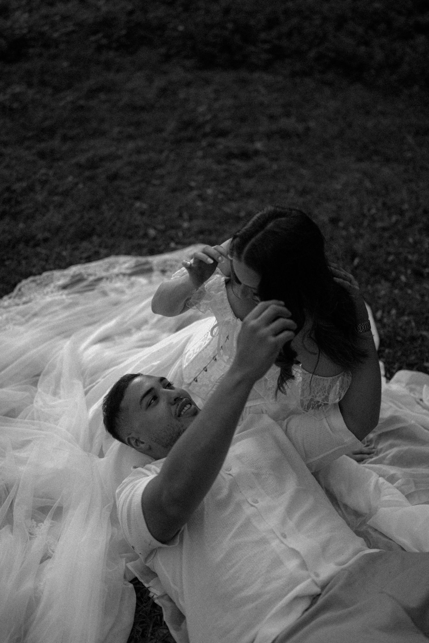 Black and white photo of bride and groom laying on grass, groom tenderly touching brides face on wedding day.