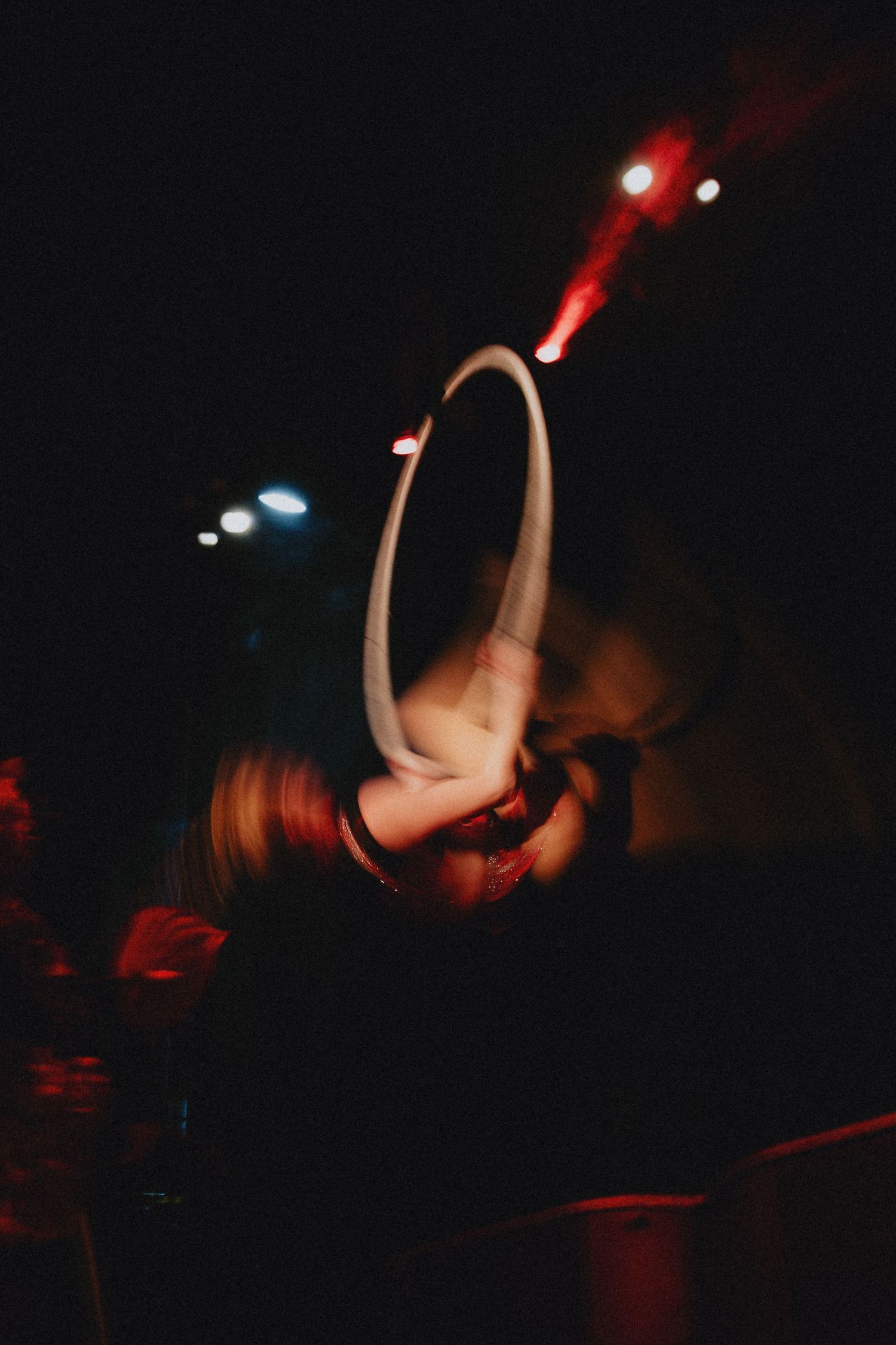 Performer spinning a hula hoop under dramatic red stage lights in a dark venue.