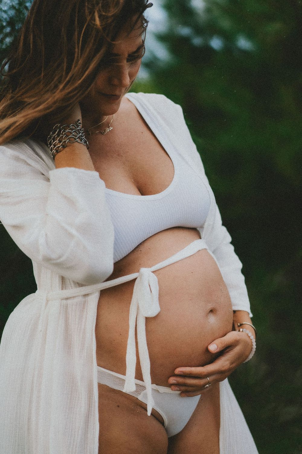 Artistic maternity photo series showing a woman in white against green foliage background.