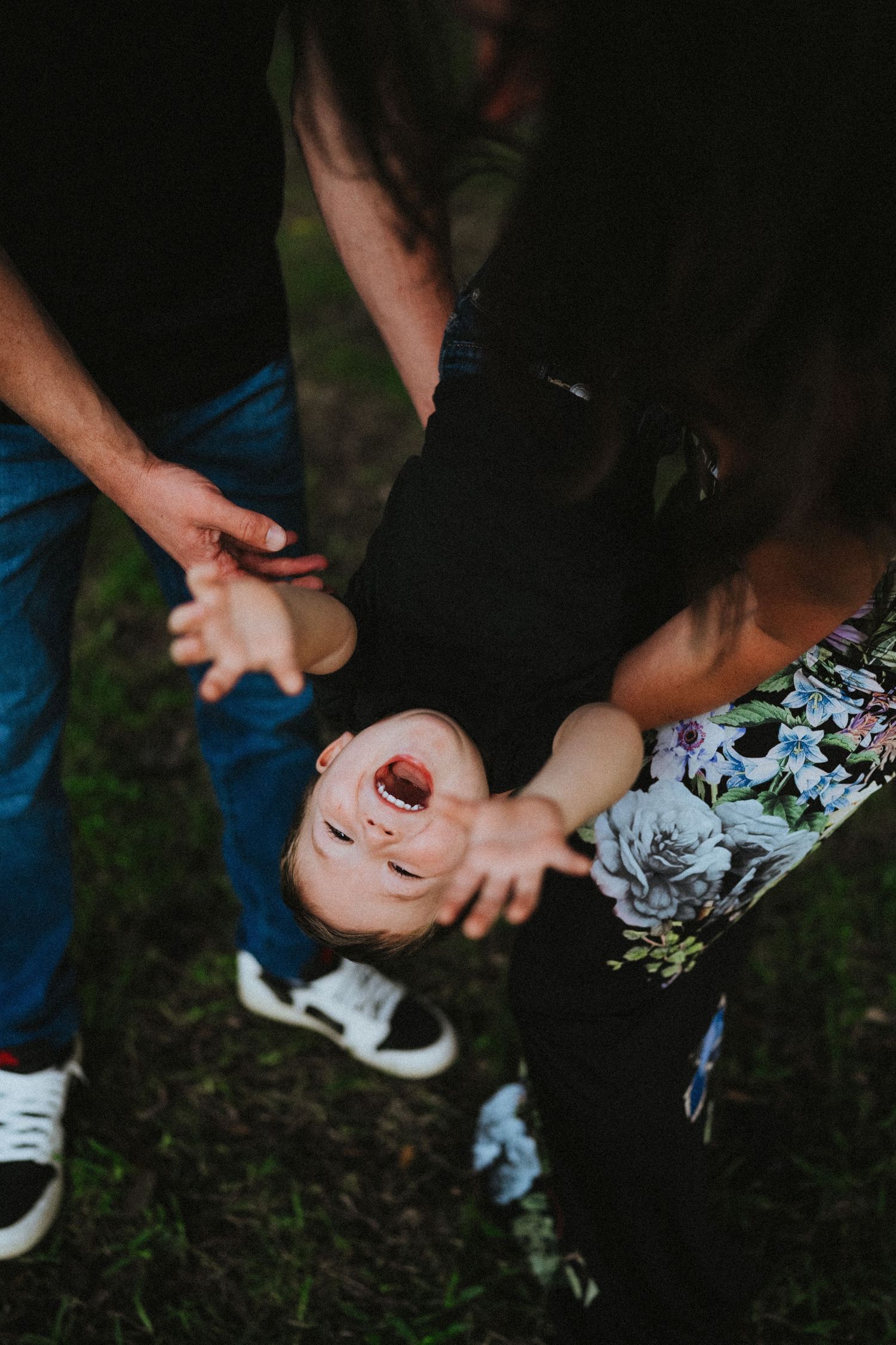 A playful moment captured outdoors with hands holding and swinging someone upside down over grass.