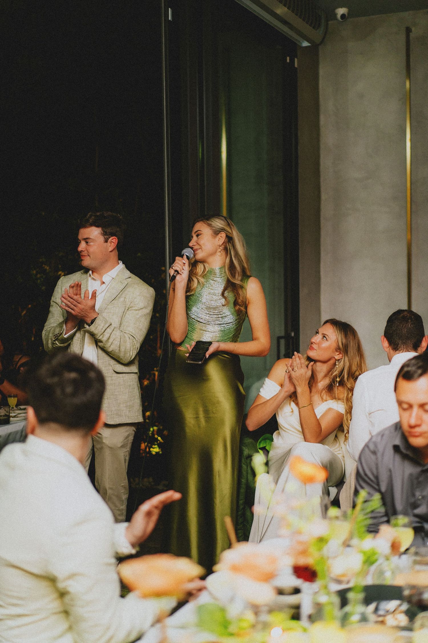 Bridesmaid in olive green gown delivering a heartfelt speech at a wedding reception dinner.