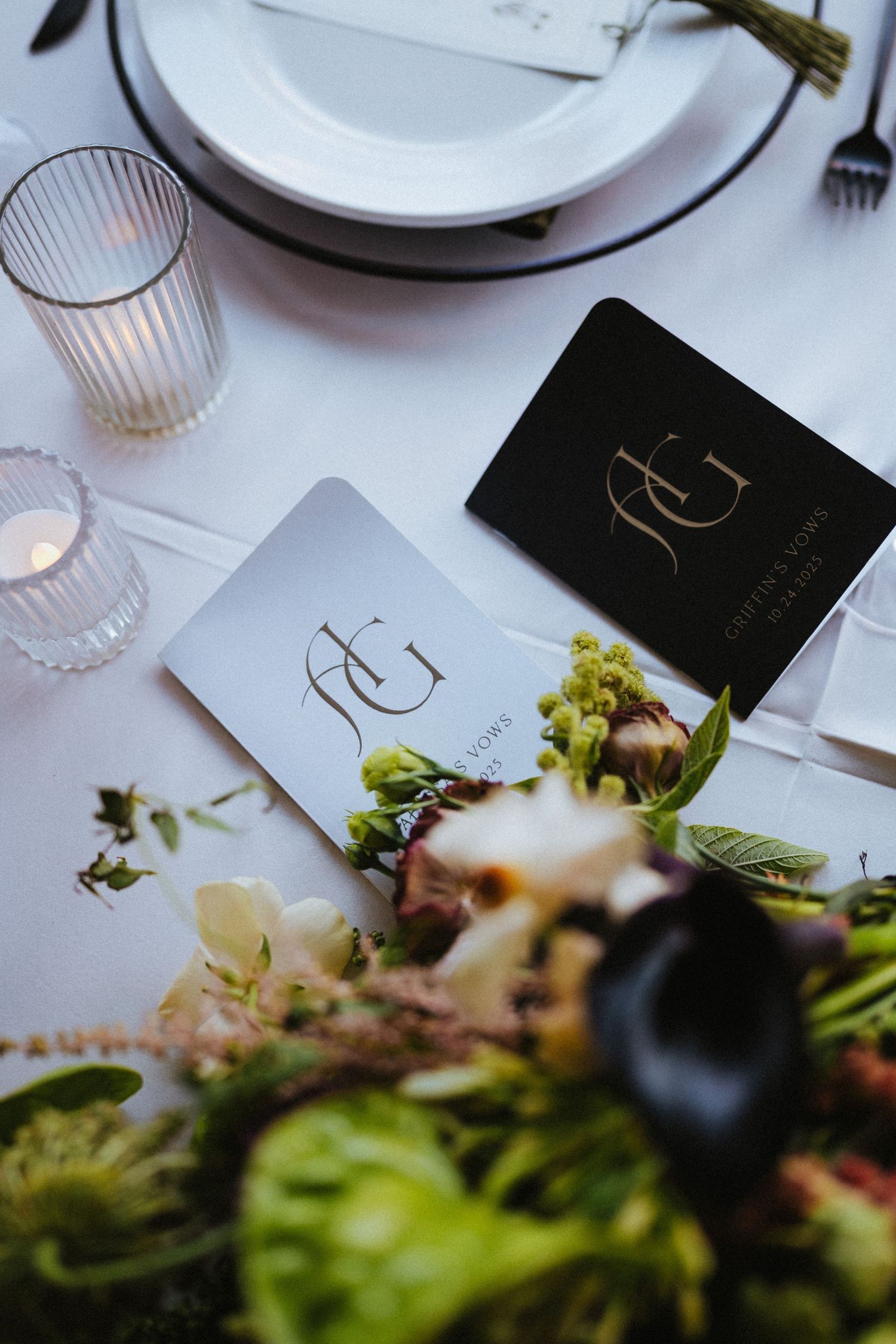 Wedding place settings with monogrammed black and white stationery cards beside fresh floral centerpieces.