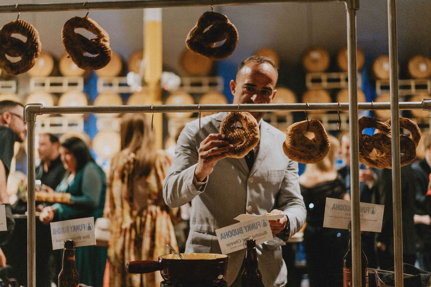 Man enthusiastically eating a large pretzel at a food festival with barrels and hanging pretzels in background.