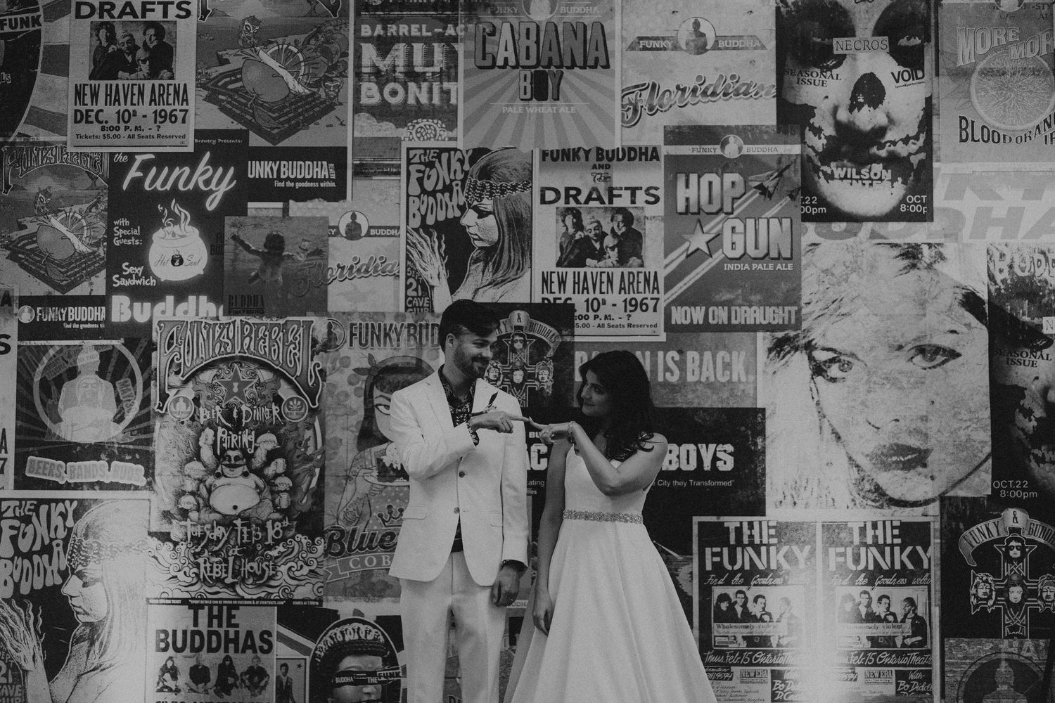 Couple poses in front of a wall covered in vintage black and white concert posters at their wedding.