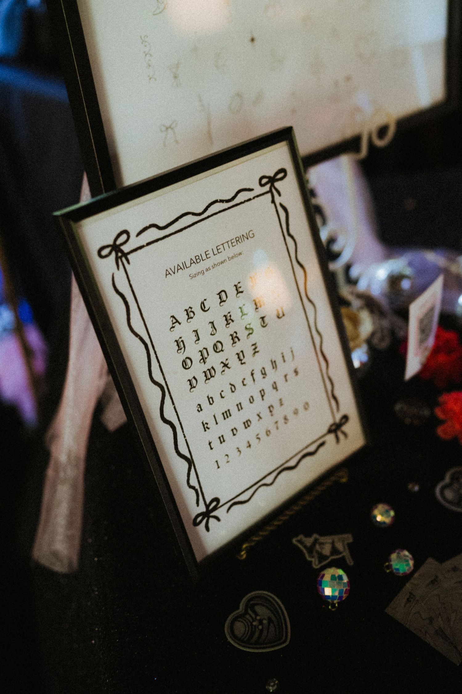Framed alphabet display showing available lettering styles with decorative border, displayed at a craft or vendor booth.