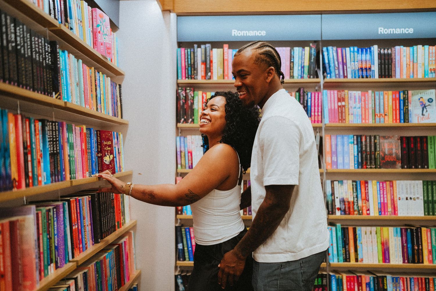 Couple browsing books together in a colorful bookstore, smiling and embracing in the romance section.