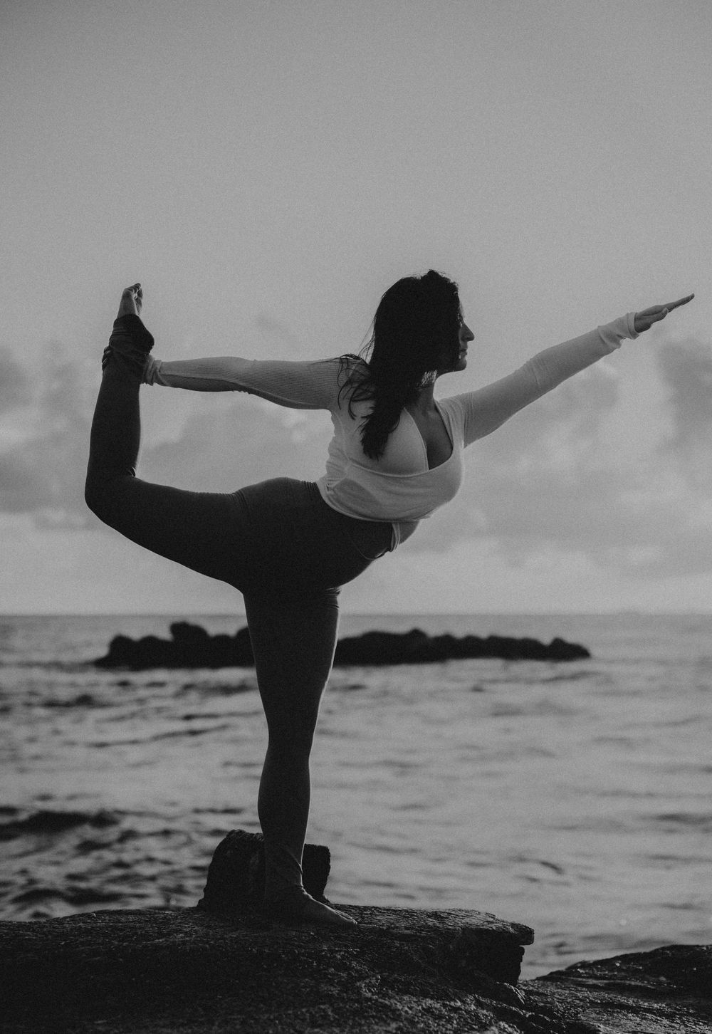 Silhouette of a person practicing yoga poses by the ocean at dusk.