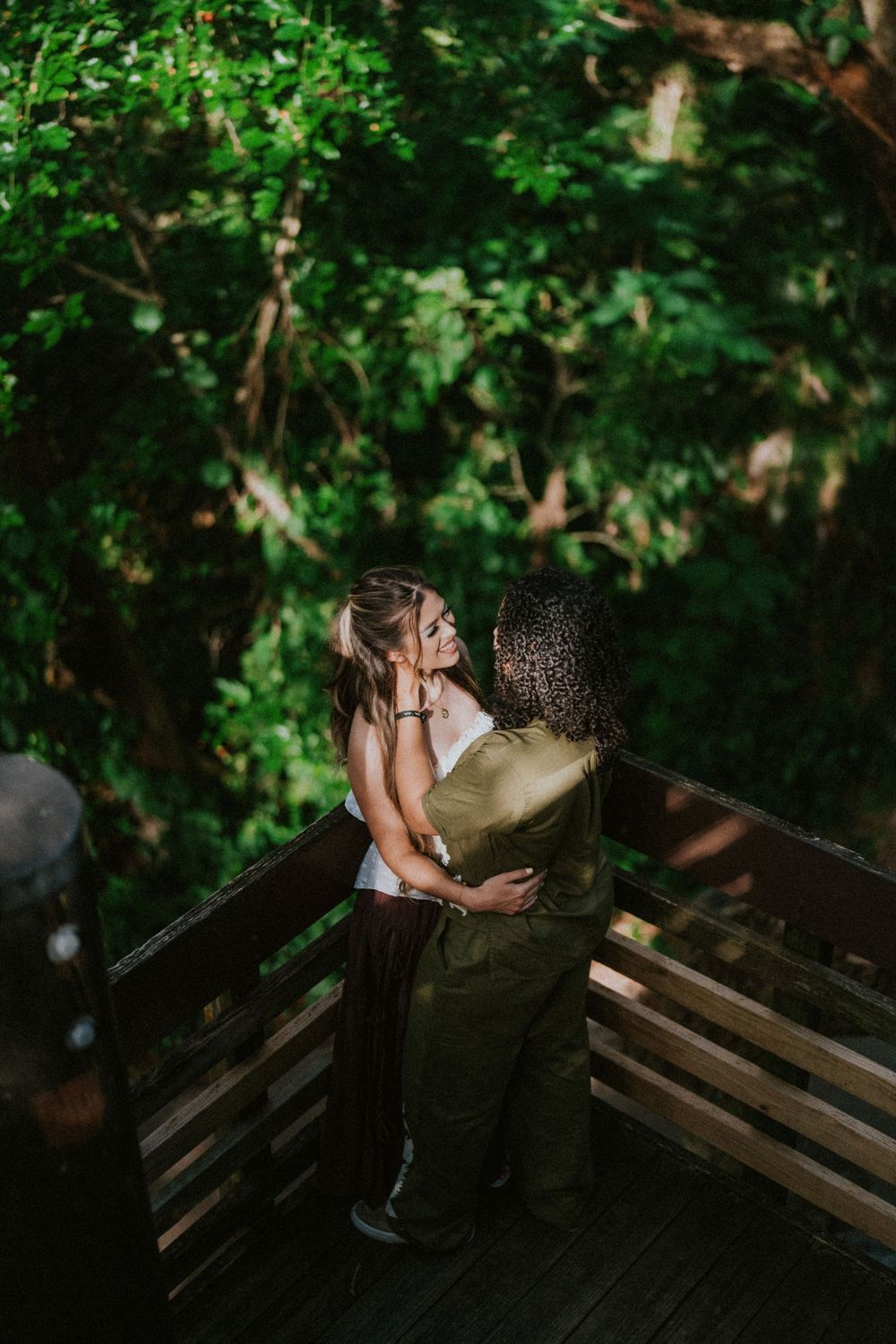 Couple embracing on wooden deck surrounded by lush green foliage.