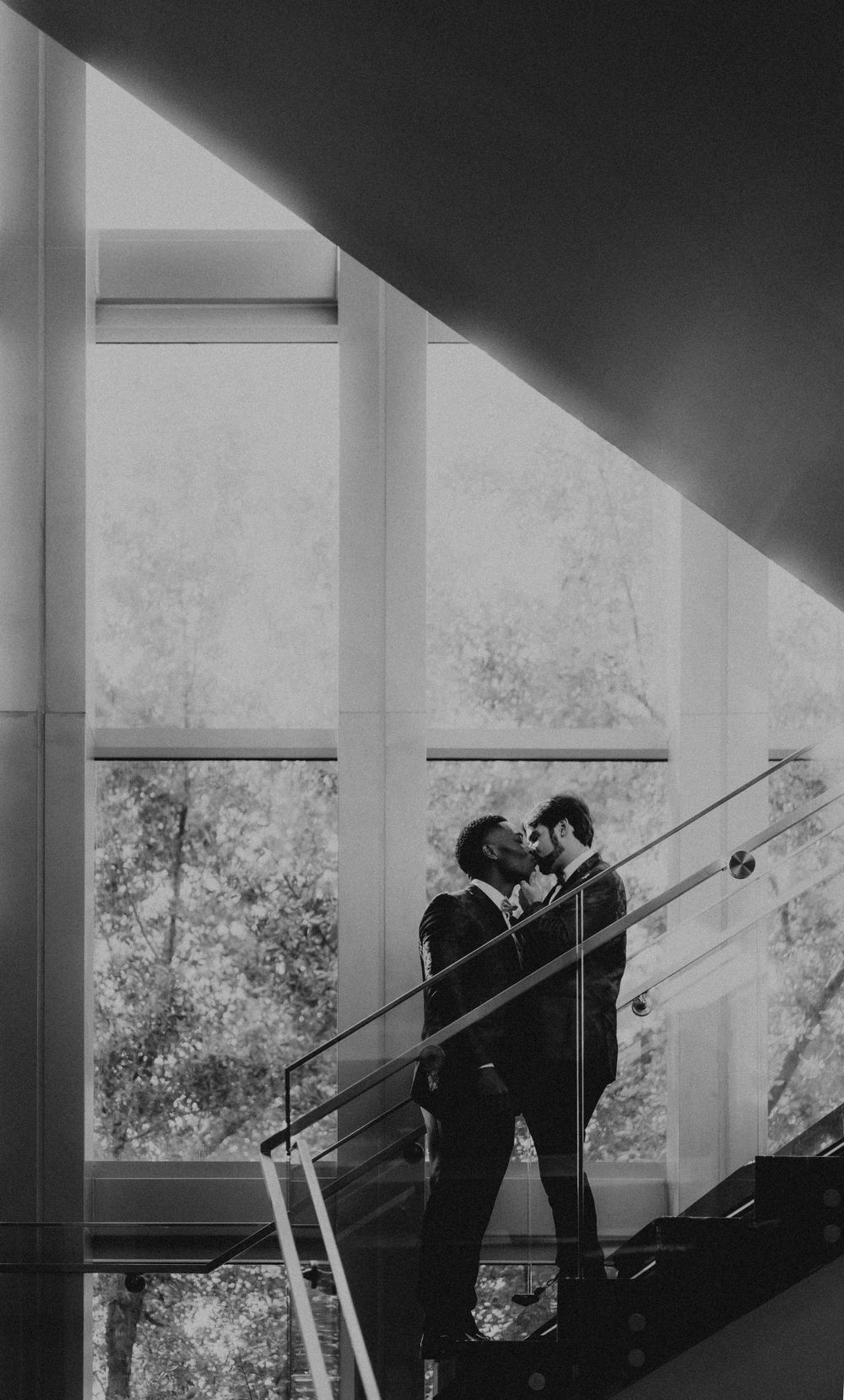 Black and white silhouette of figures standing on stairs against bright windows.