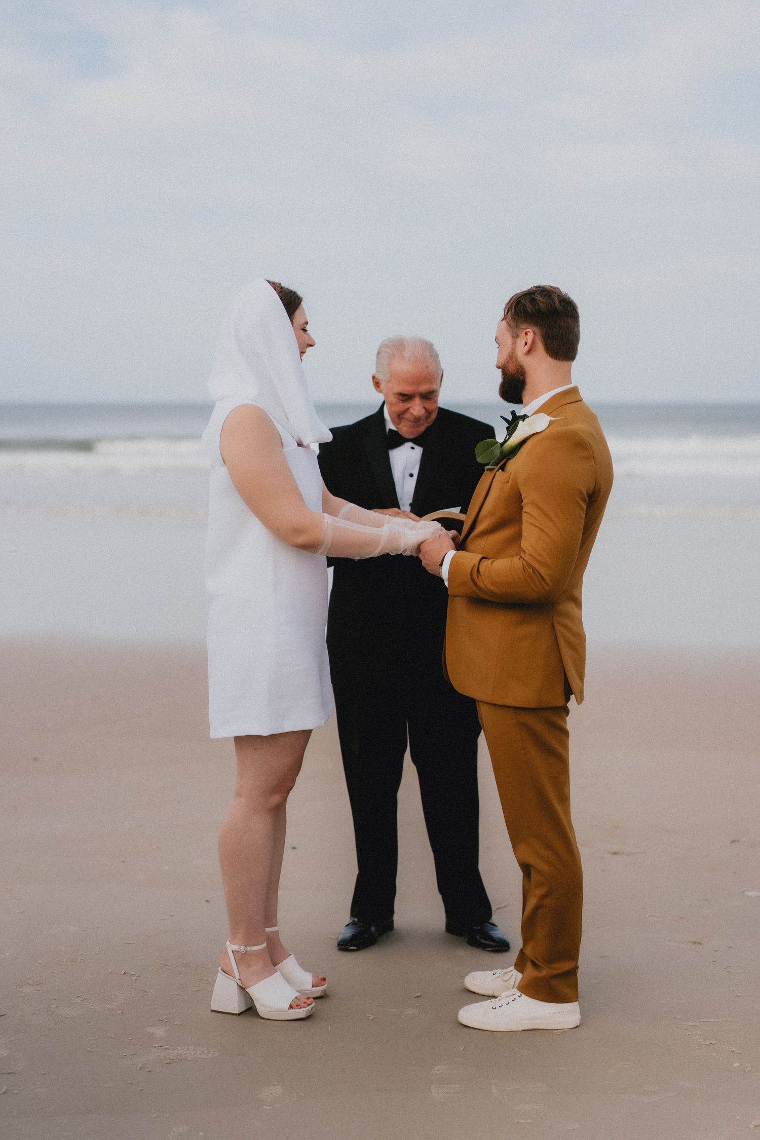 Bride and groom exchange vows with officiant on a sandy beach wedding ceremony by the ocean.