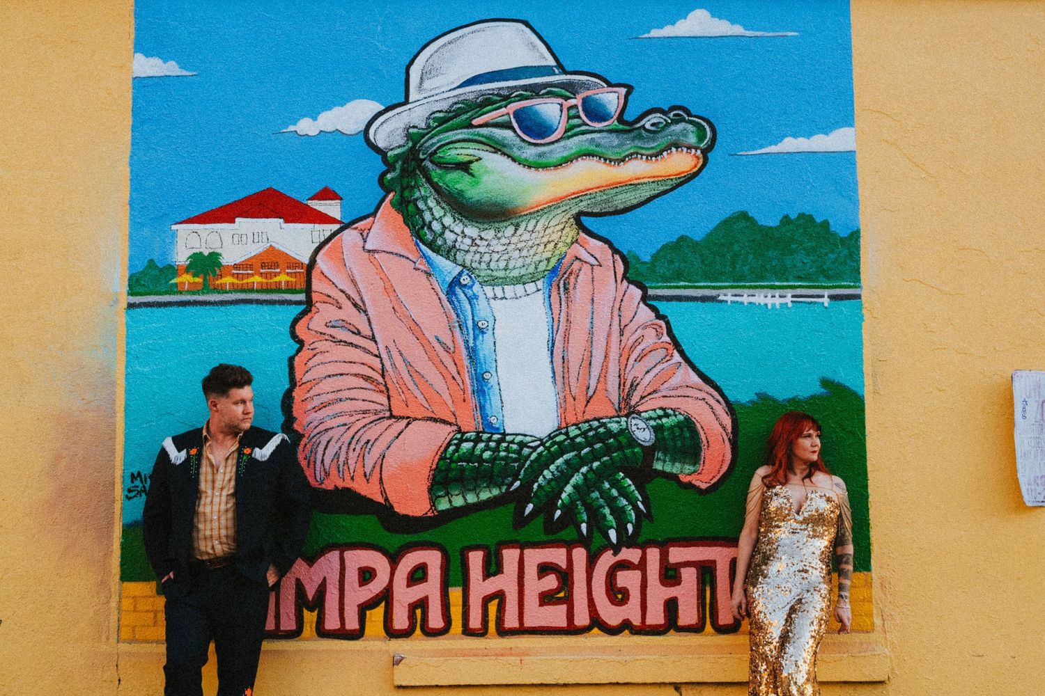 Couple poses beside colorful Tampa Heights mural featuring a stylish alligator in a pink blazer and hat.