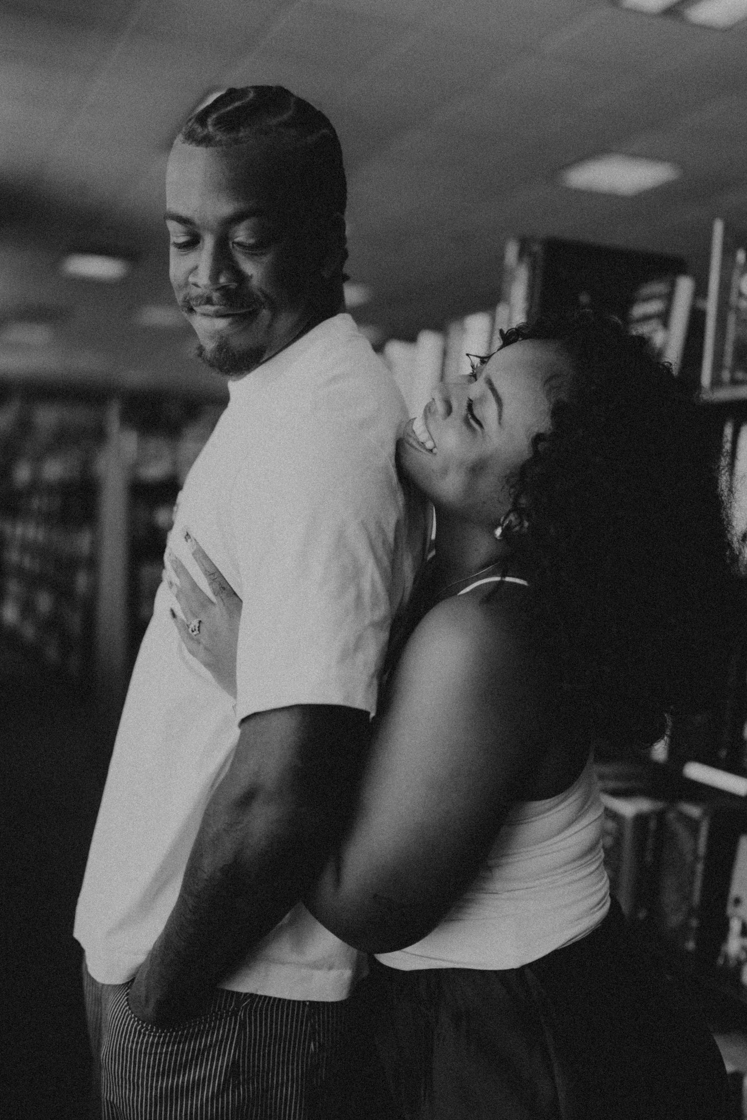 A black and white photo of a joyful woman hugging a smiling man from behind in a bookstore.