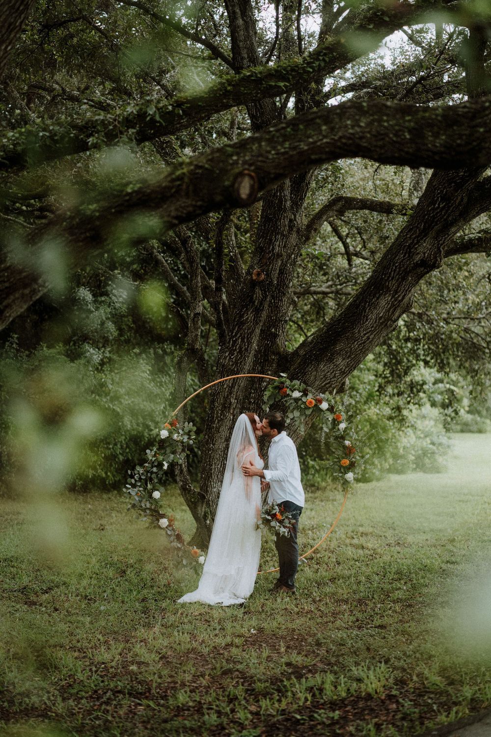 Romantic wedding couple poses under a large tree decorated with floral arrangements.