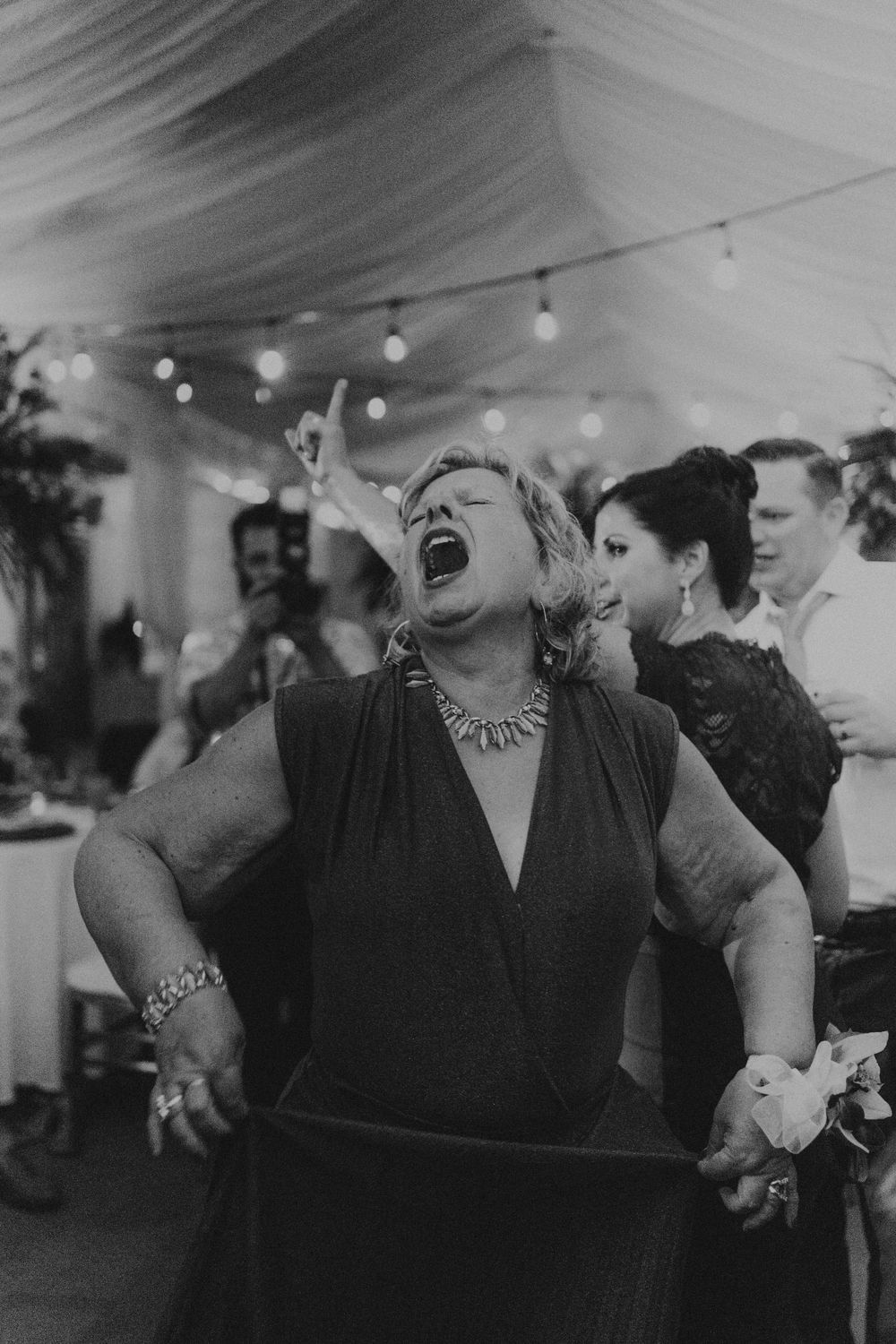 Wedding reception guests laughing and celebrating together under indoor string lights.