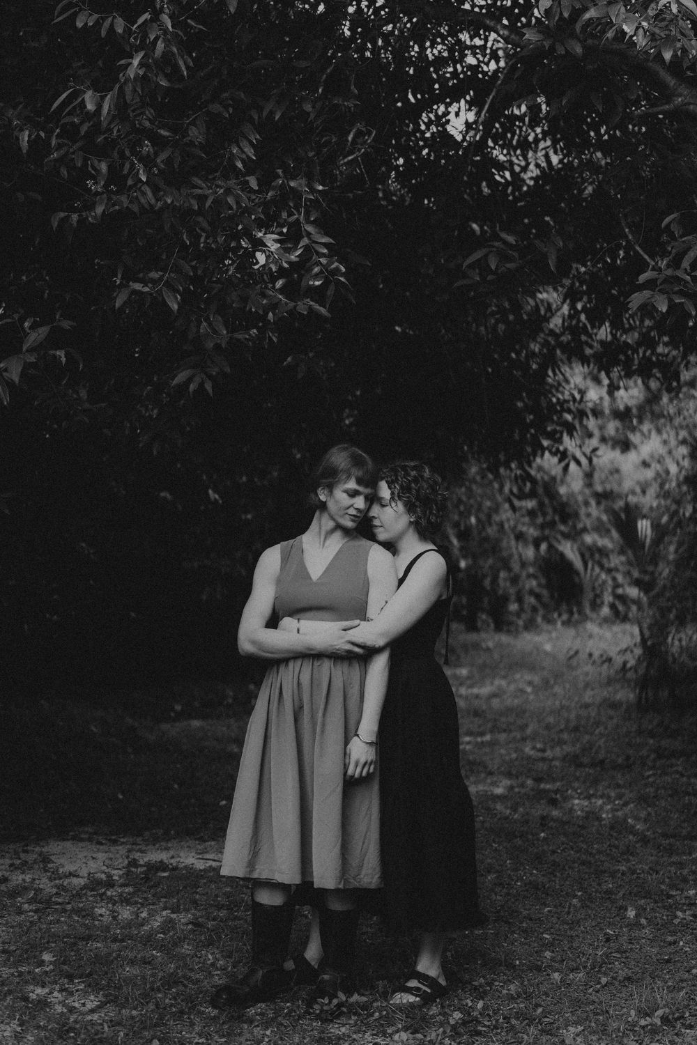 An artistic black and white photograph showing a tender moment between two people in nature.