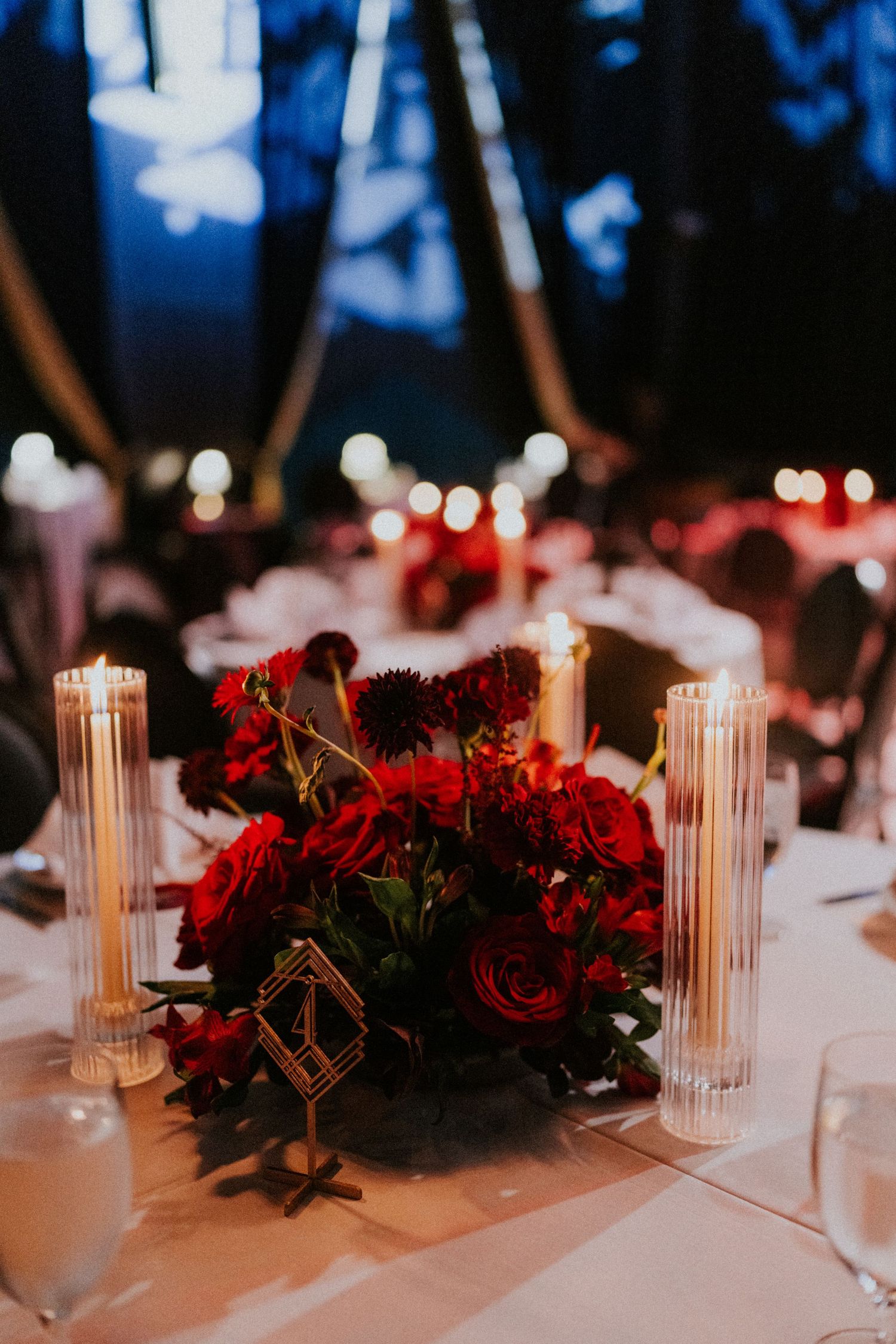 Red rose centerpiece with pillar candles on white tablecloth at elegant evening wedding reception.