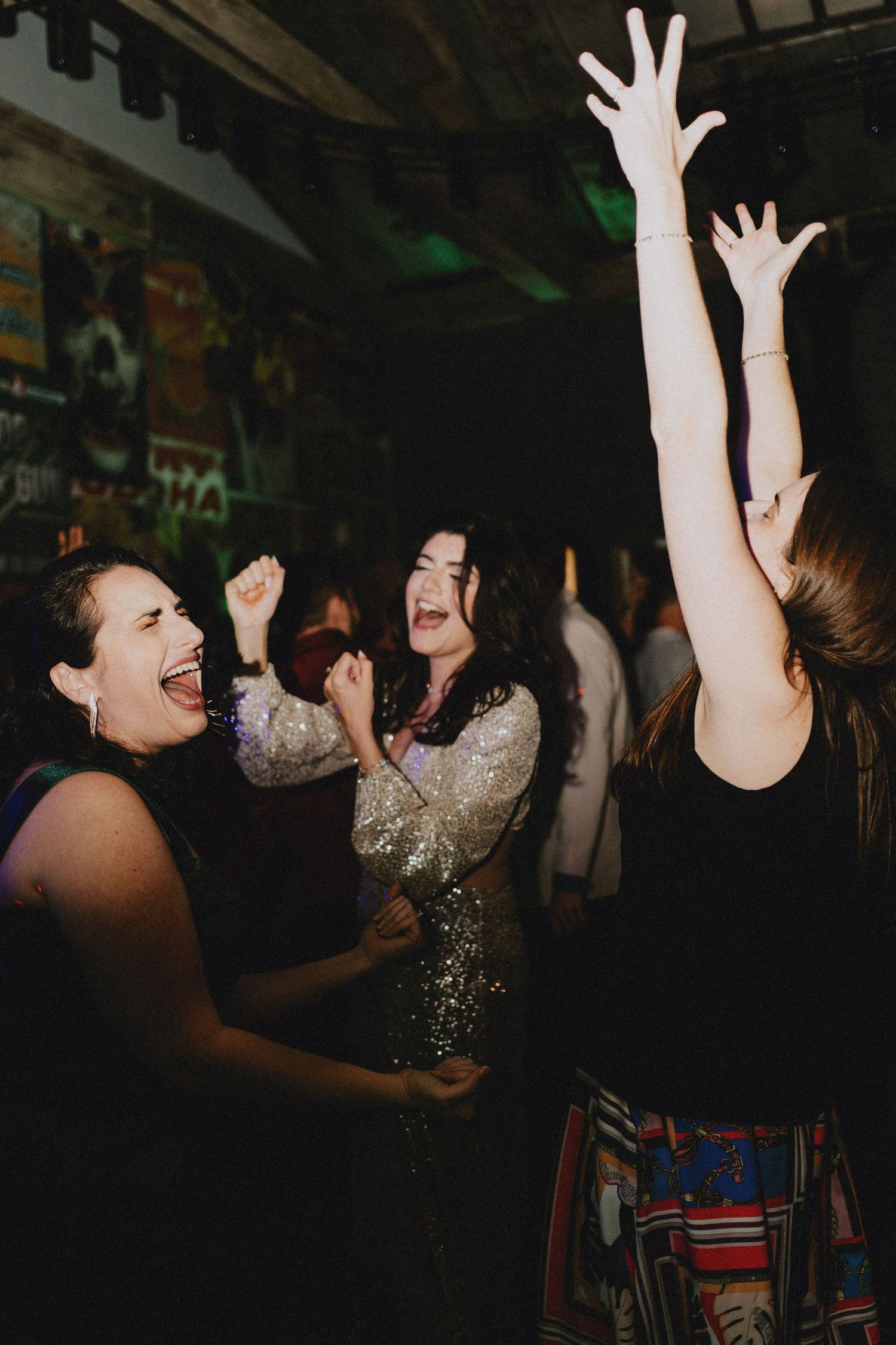 Women dancing joyfully at a party, arms raised in celebration under dim lighting.