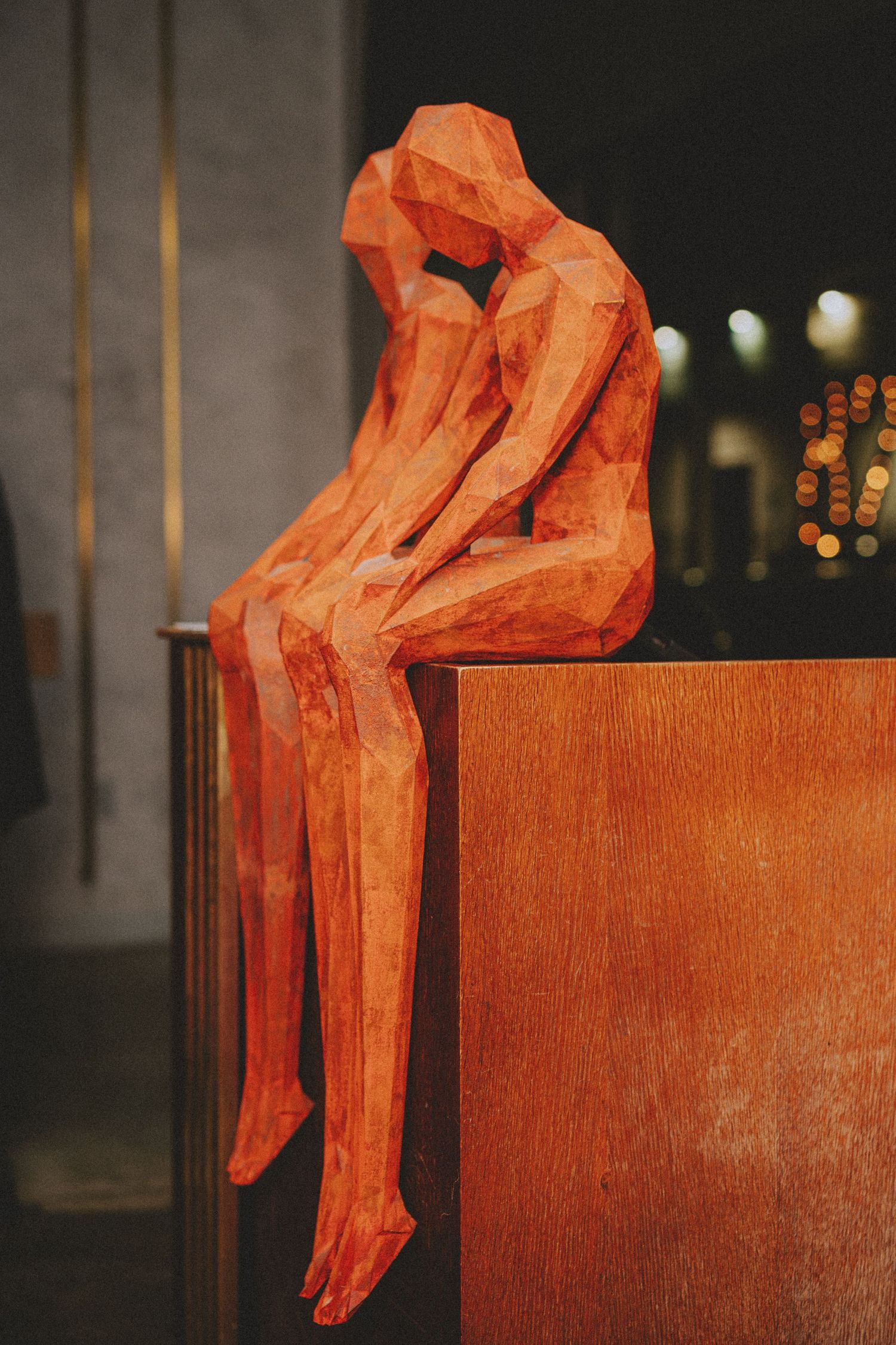 Orange geometric low-poly sculpture of seated figure perched on wooden cabinet at wedding venue.