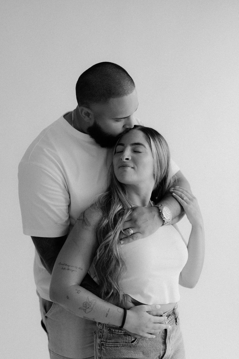 Black and white intimate portrait of a romantic couple embracing, with one person kissing the other's forehead.