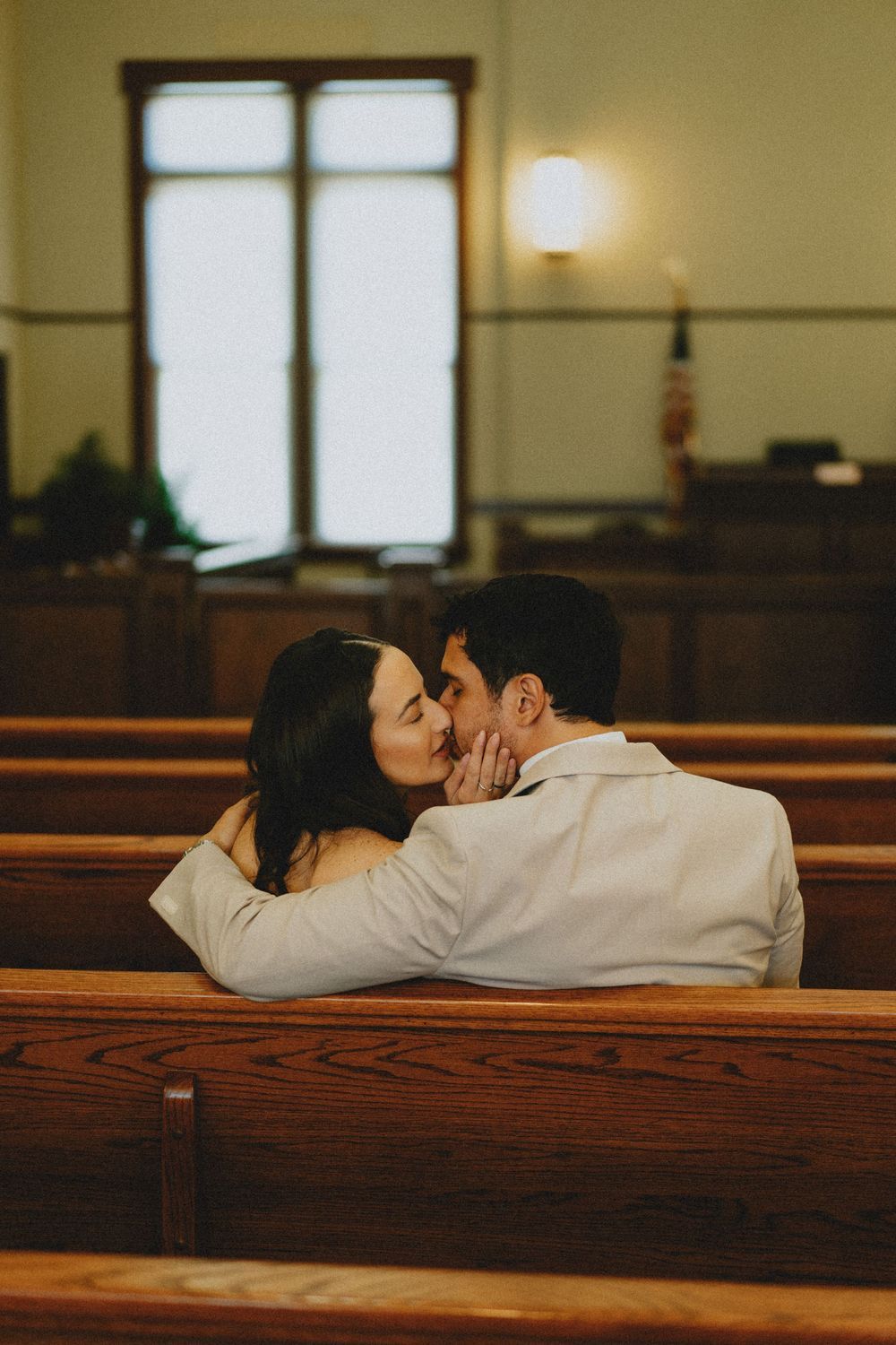 A romantic moment captured between a couple sitting in wooden church pews.