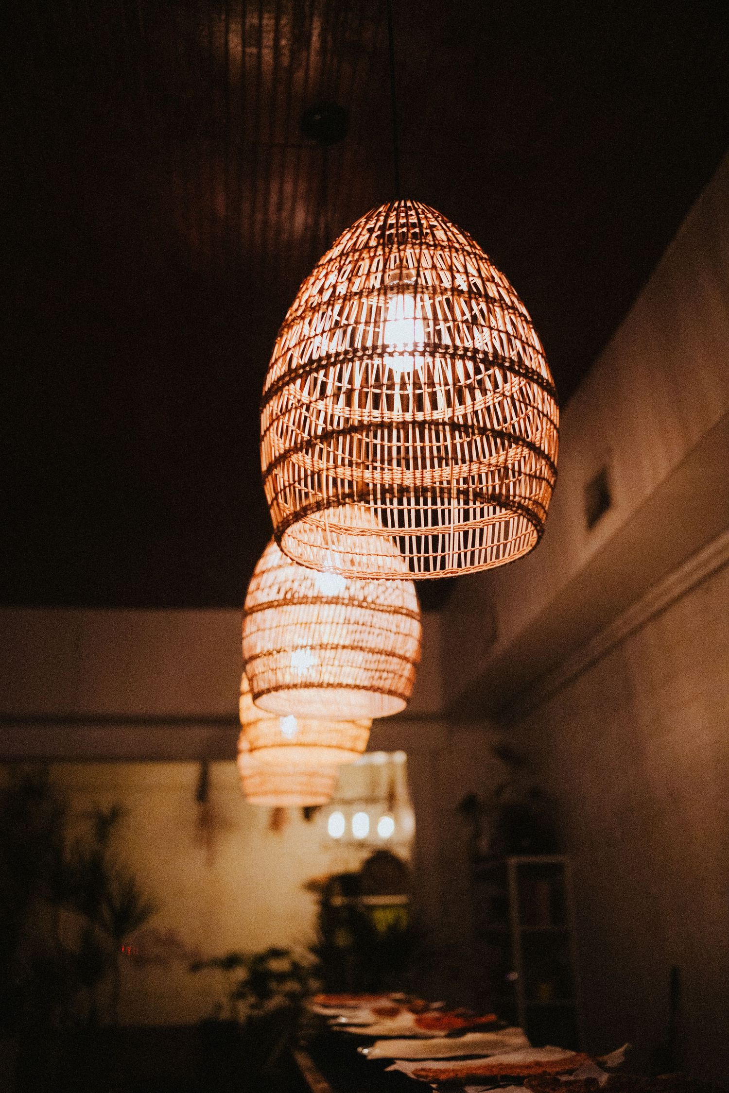 Warm woven rattan pendant lights hanging from a dark ceiling in a cozy dimly lit restaurant.