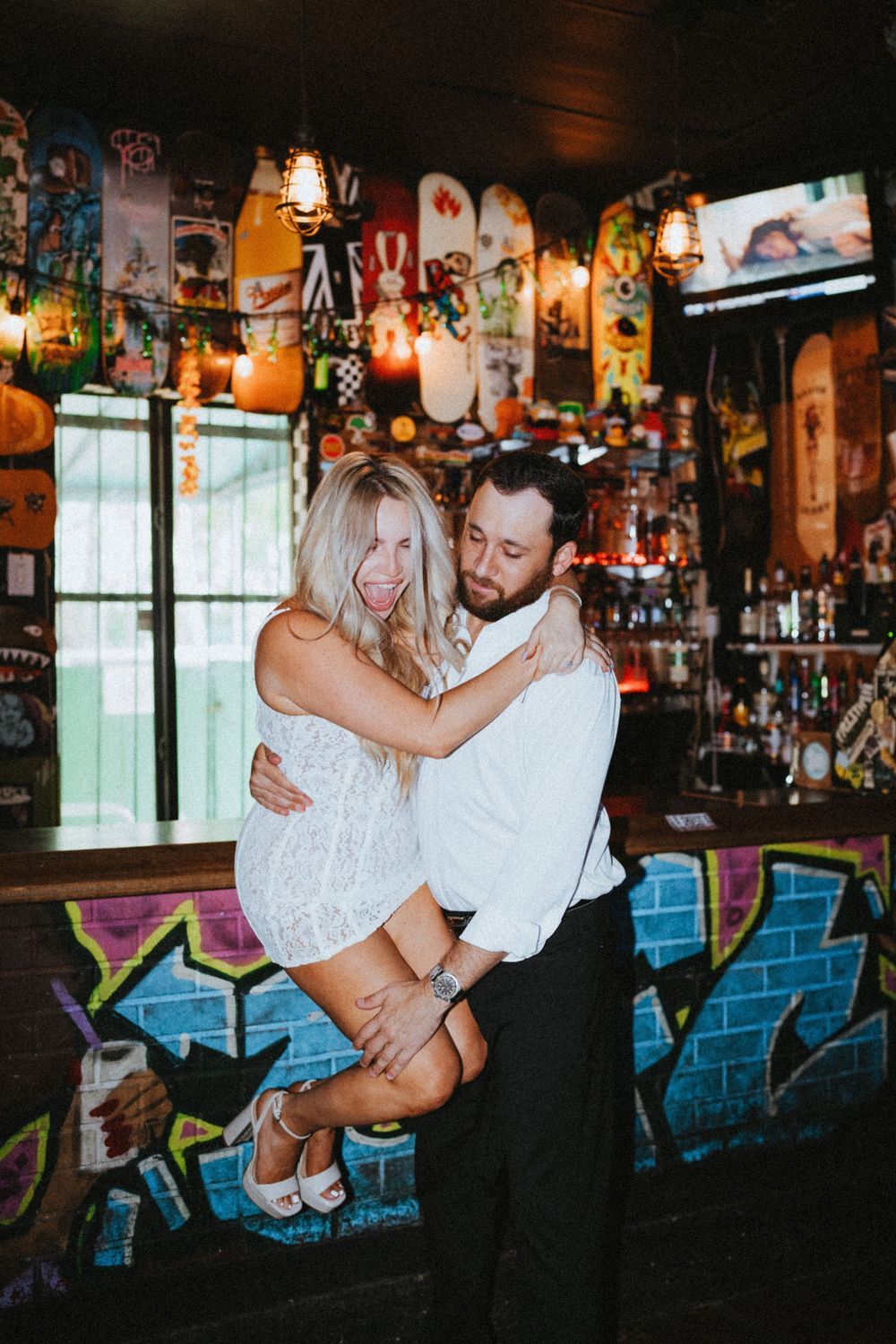 A couple shares an intimate dance moment in a dimly lit bar with graffiti walls and vintage decor.