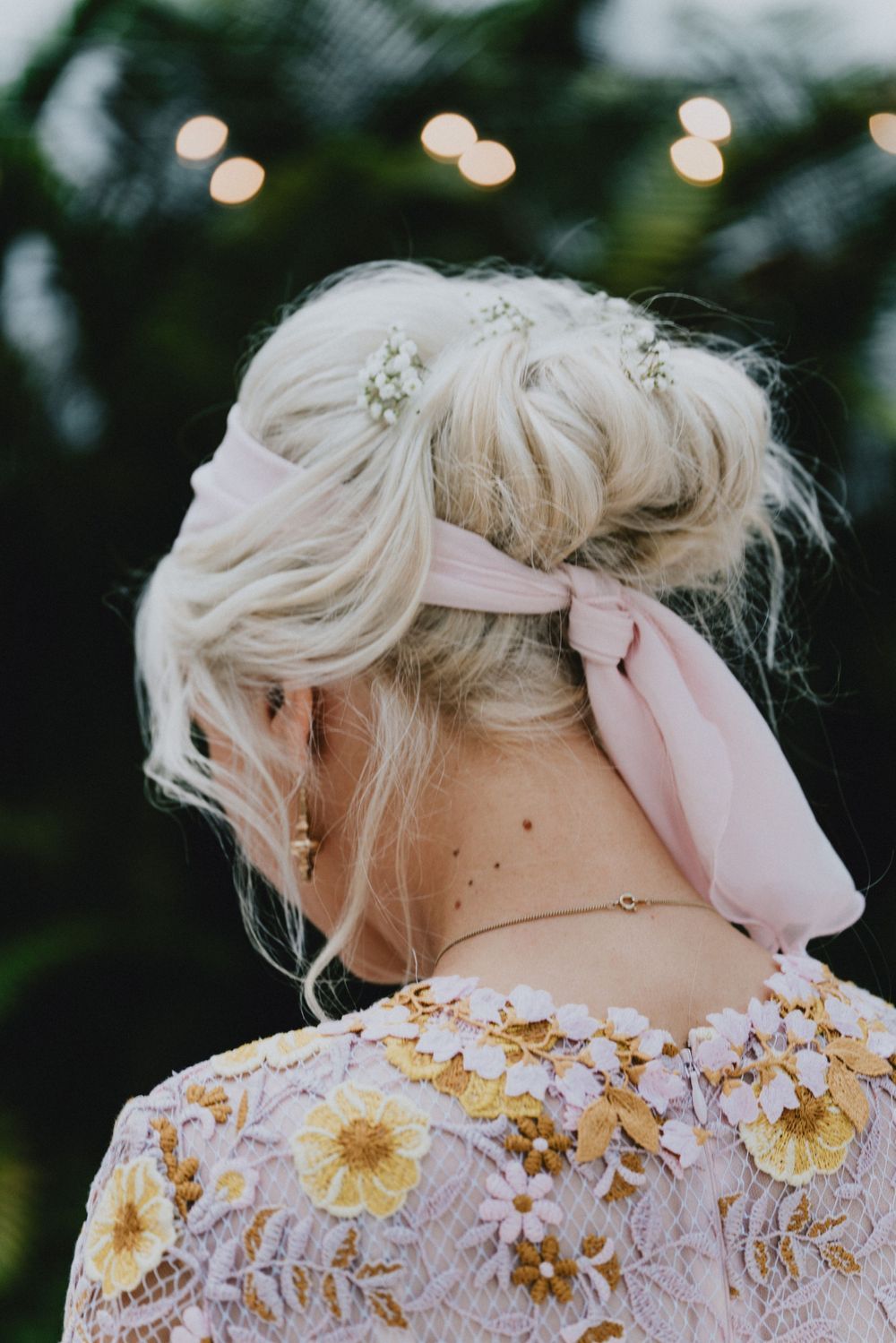 Blonde updo with pink ribbon and floral lace dress detail captured from behind.