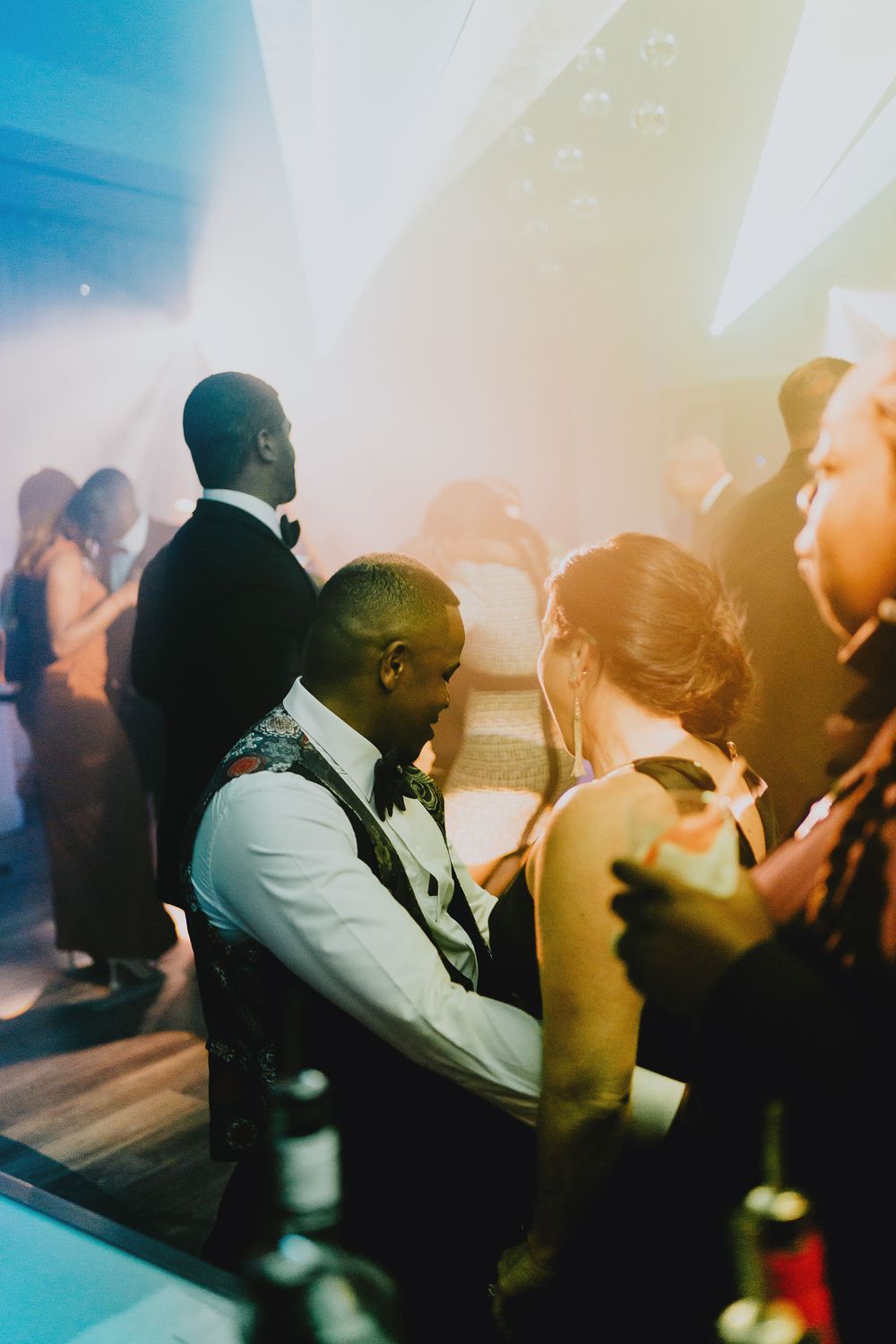 Dance party scene with silhouettes of people against colorful blue and yellow lighting.