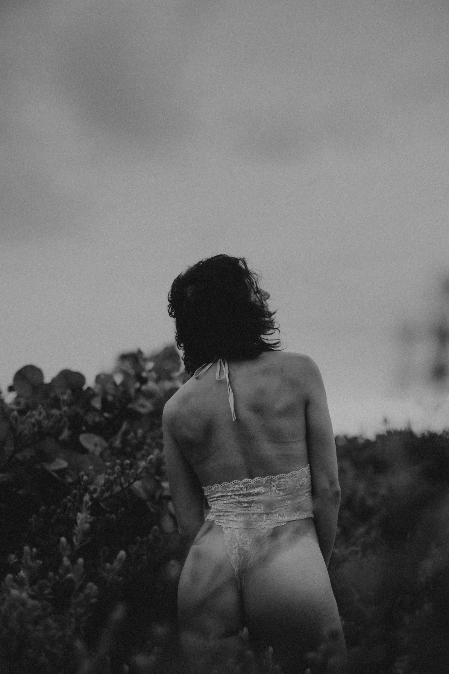 Dreamy monochrome outdoor portrait against a cloudy sky.