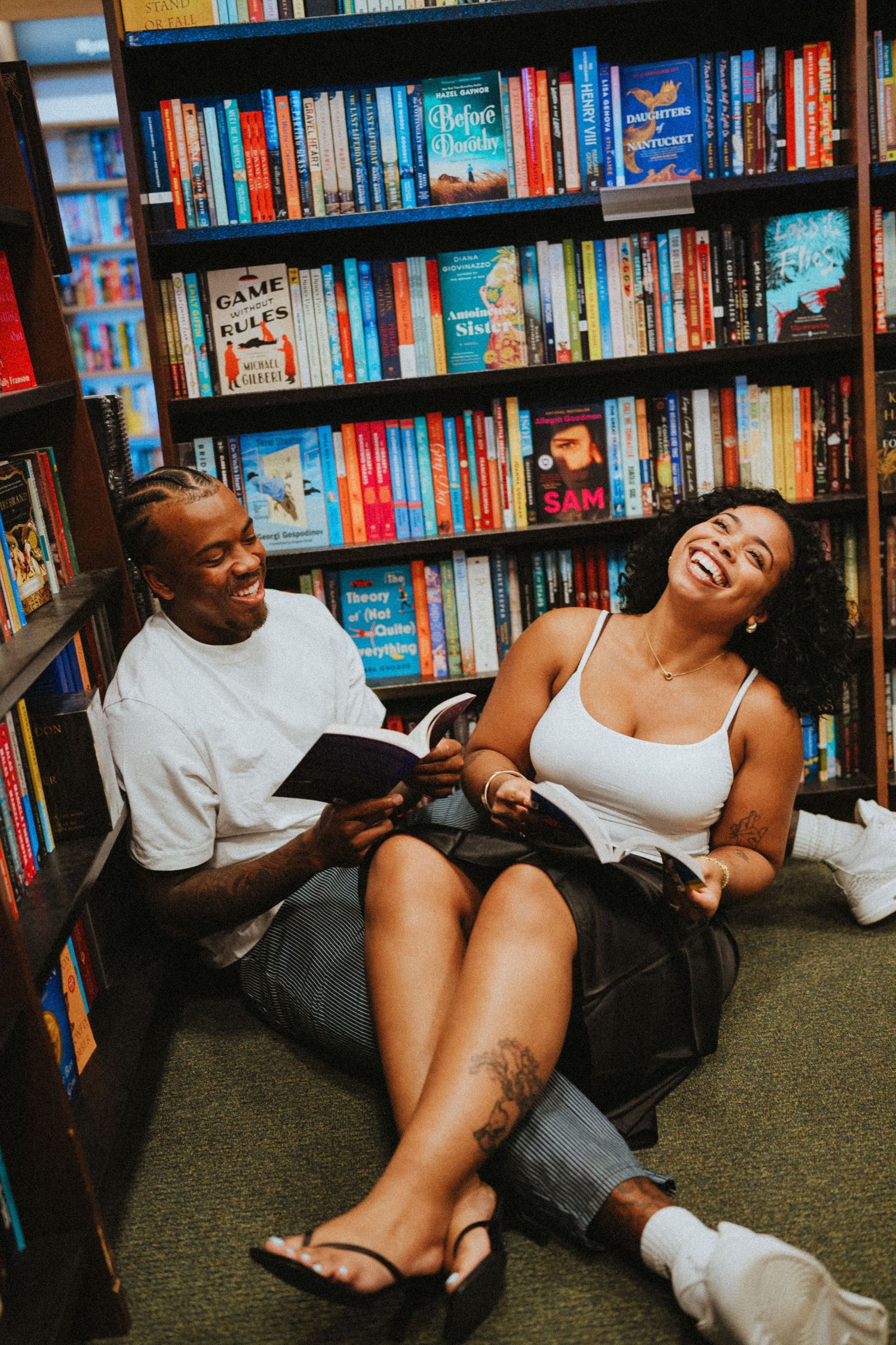 Couple laughing and reading together on a bookstore floor surrounded by colorful bookshelves.