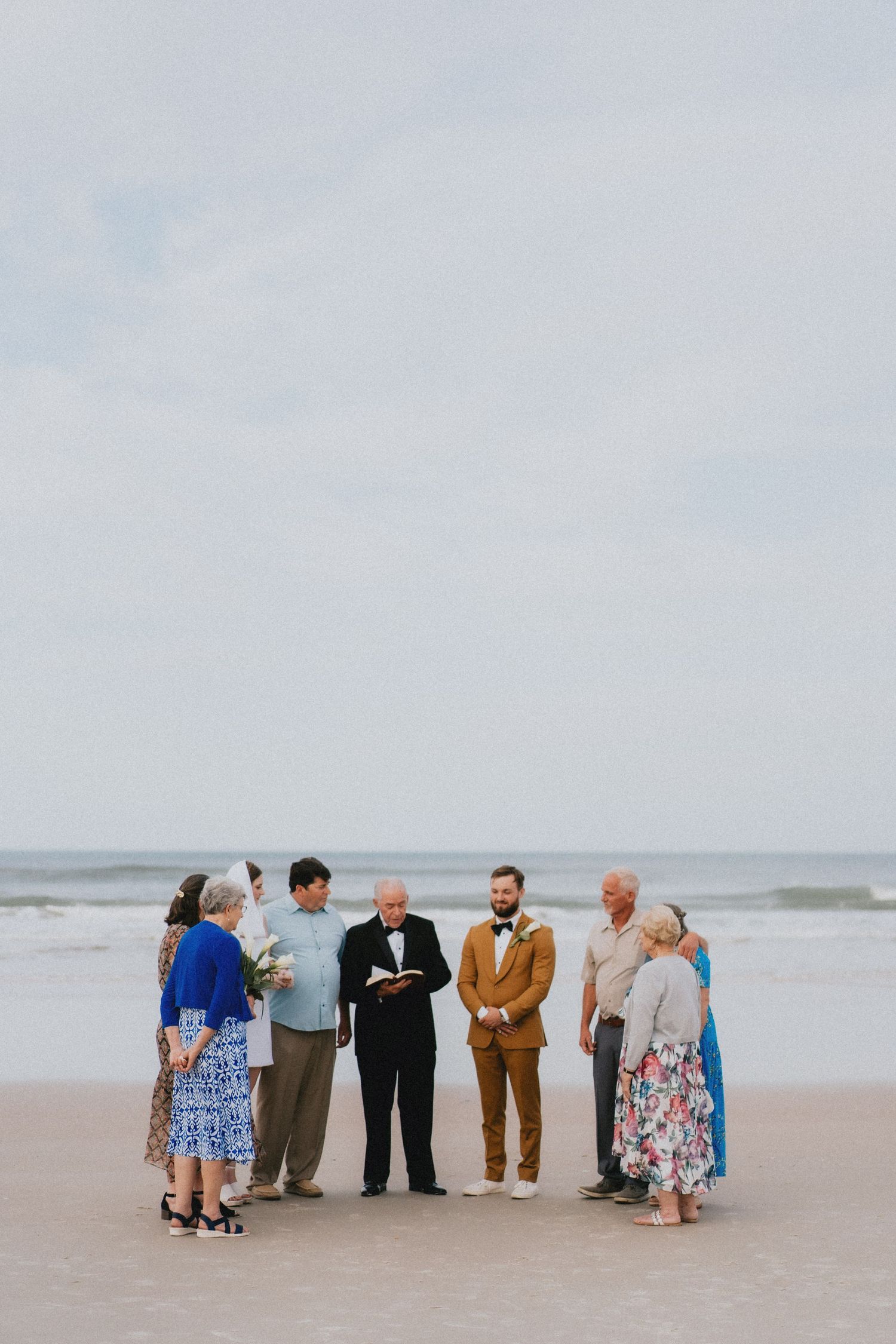 Small intimate beach wedding ceremony with couple, officiant, and family gathered by the ocean.