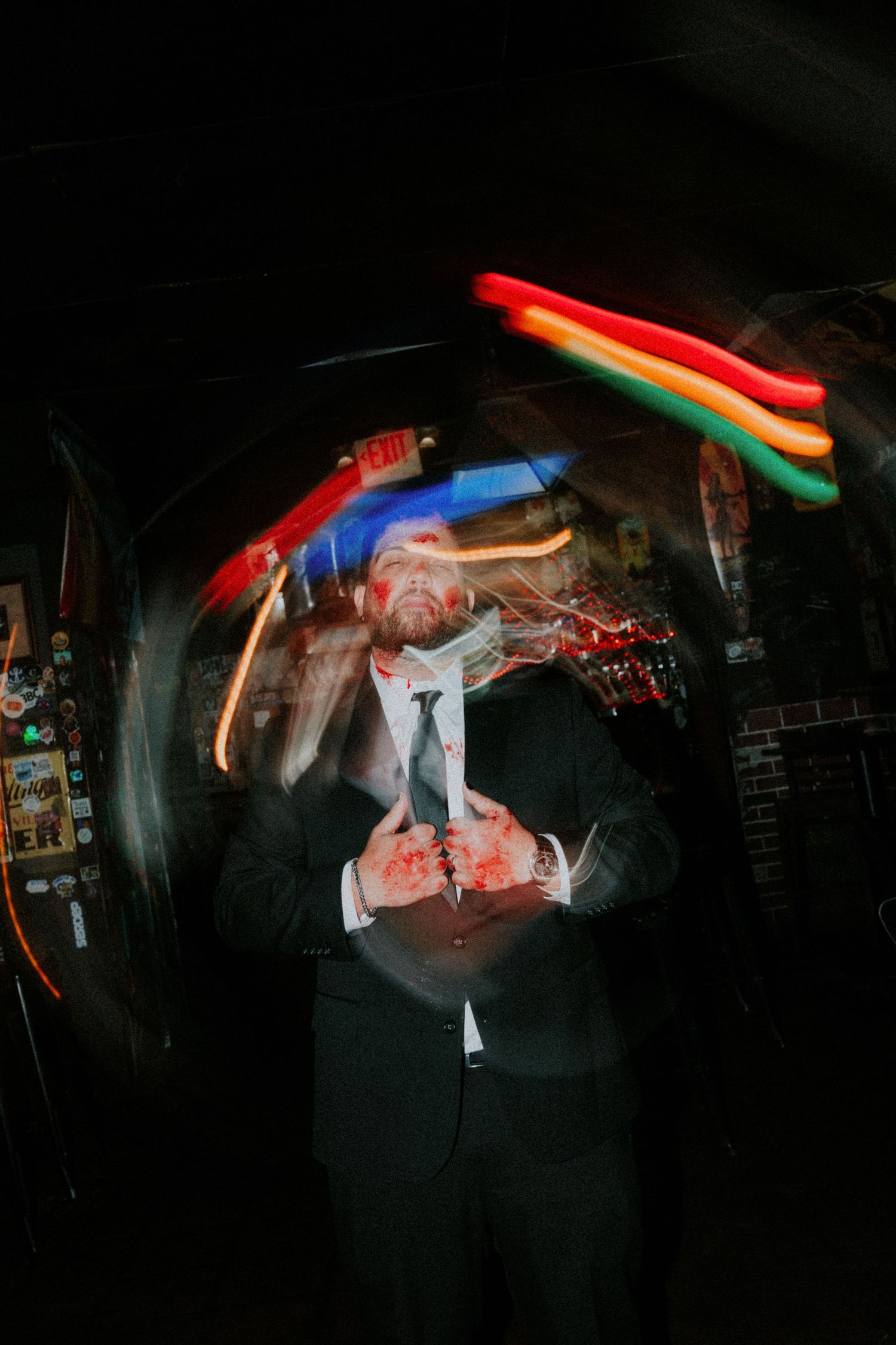 Man in suit with colorful neon light trails swirling around him in a dark bar setting.