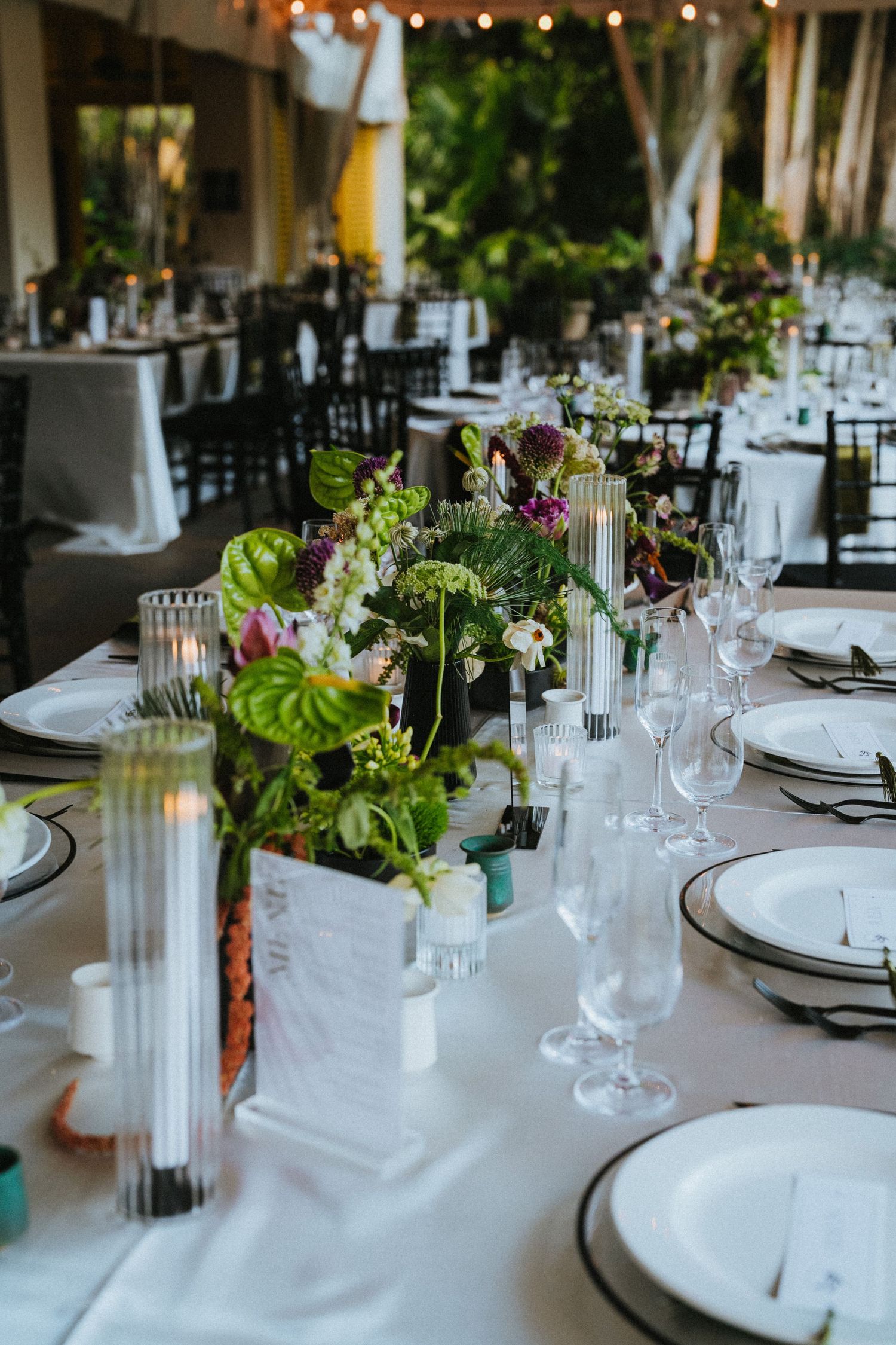 Elegant wedding reception table set with lush green floral centerpieces, candles, and crystal glassware on white linen.