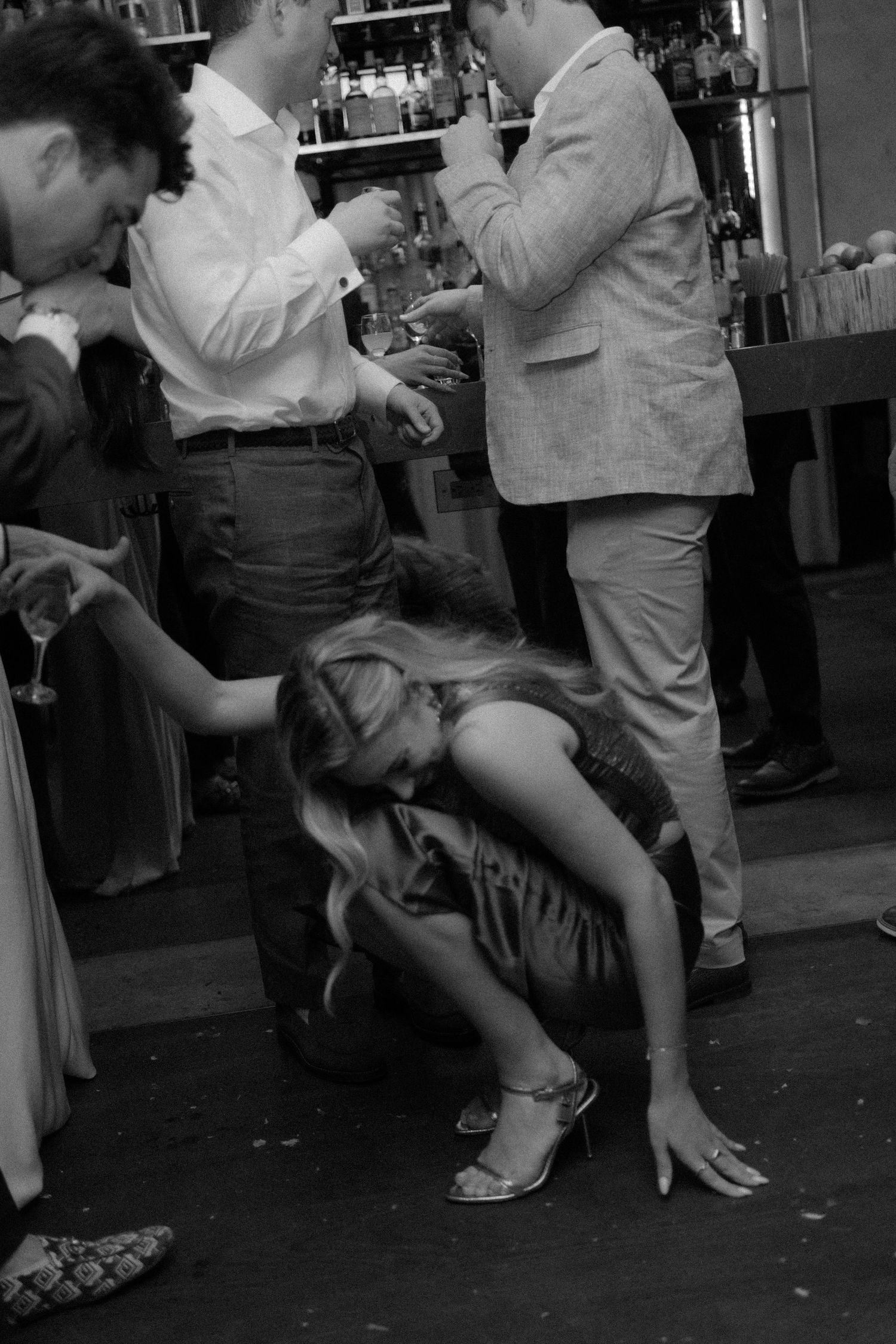 Black and white photo of wedding guests dancing and socializing at a lively reception bar area.
