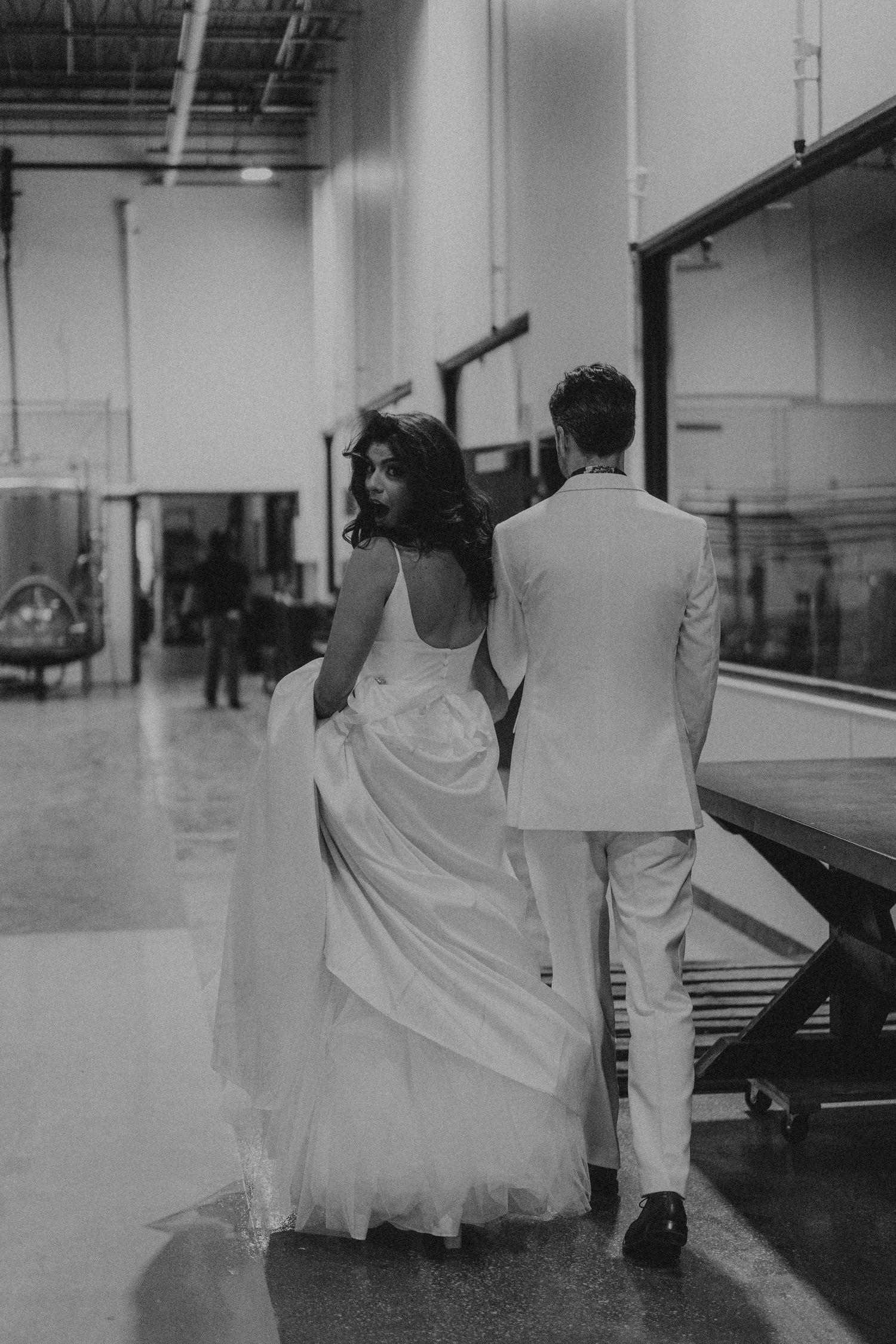 Black and white photo of bride and groom walking through an industrial wedding venue.