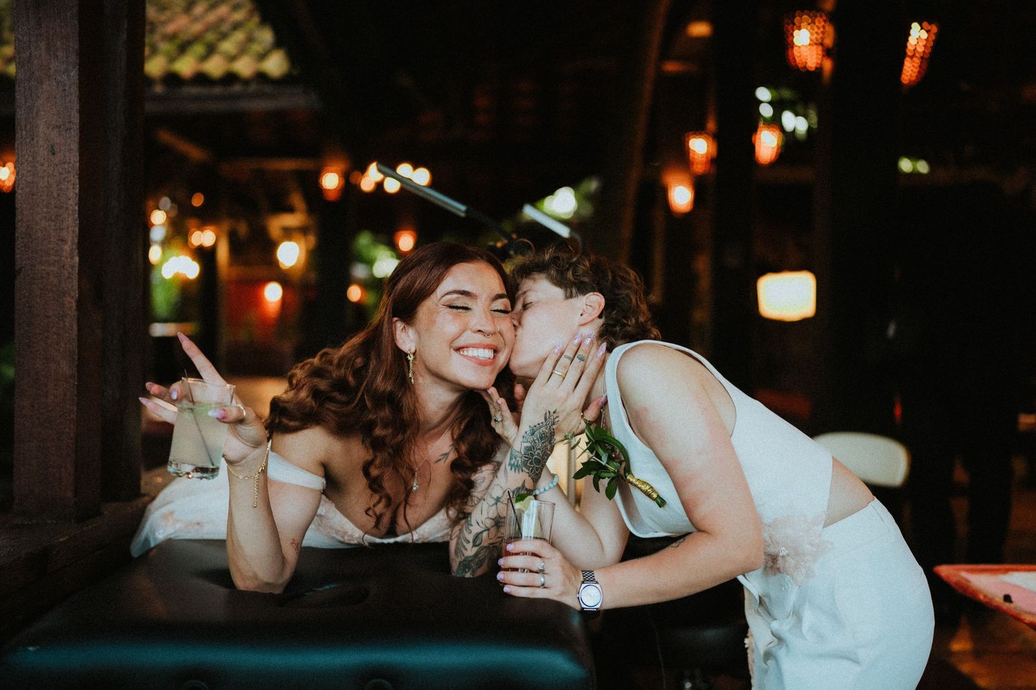 Two women sharing a tender moment at a romantic outdoor restaurant with warm glowing lanterns at night.