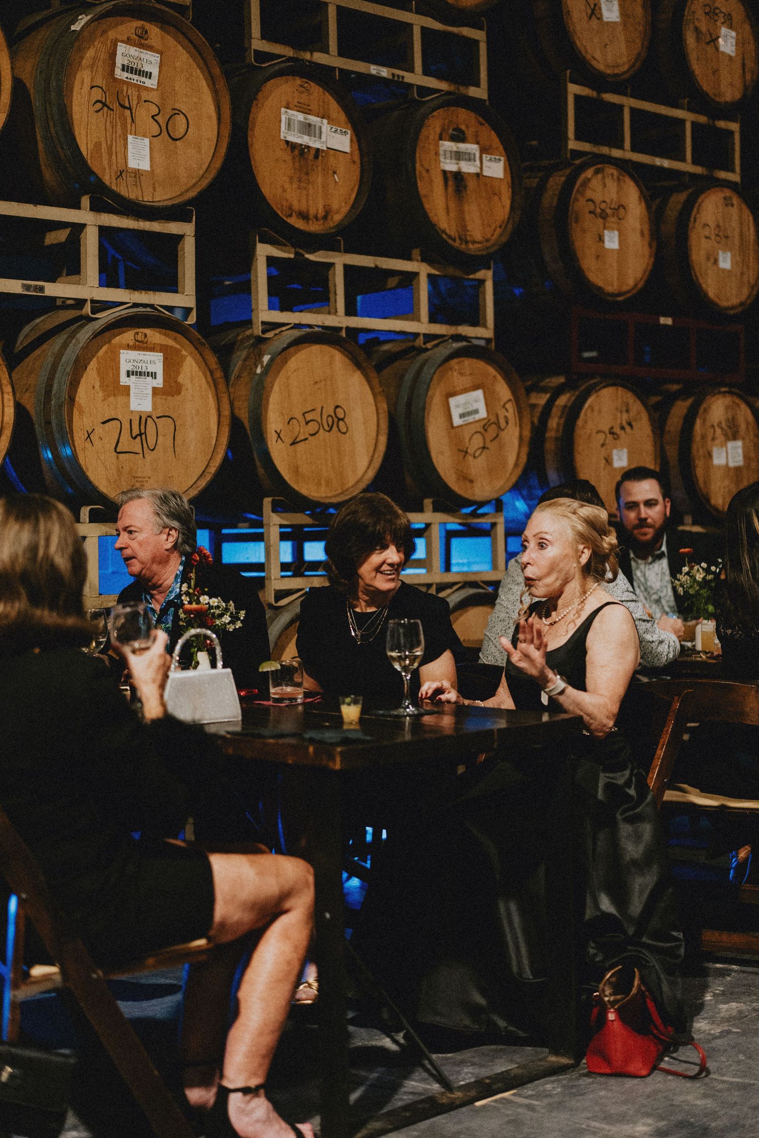 Guests socializing at a winery event surrounded by oak barrels, enjoying wine in an elegant dimly lit cellar.