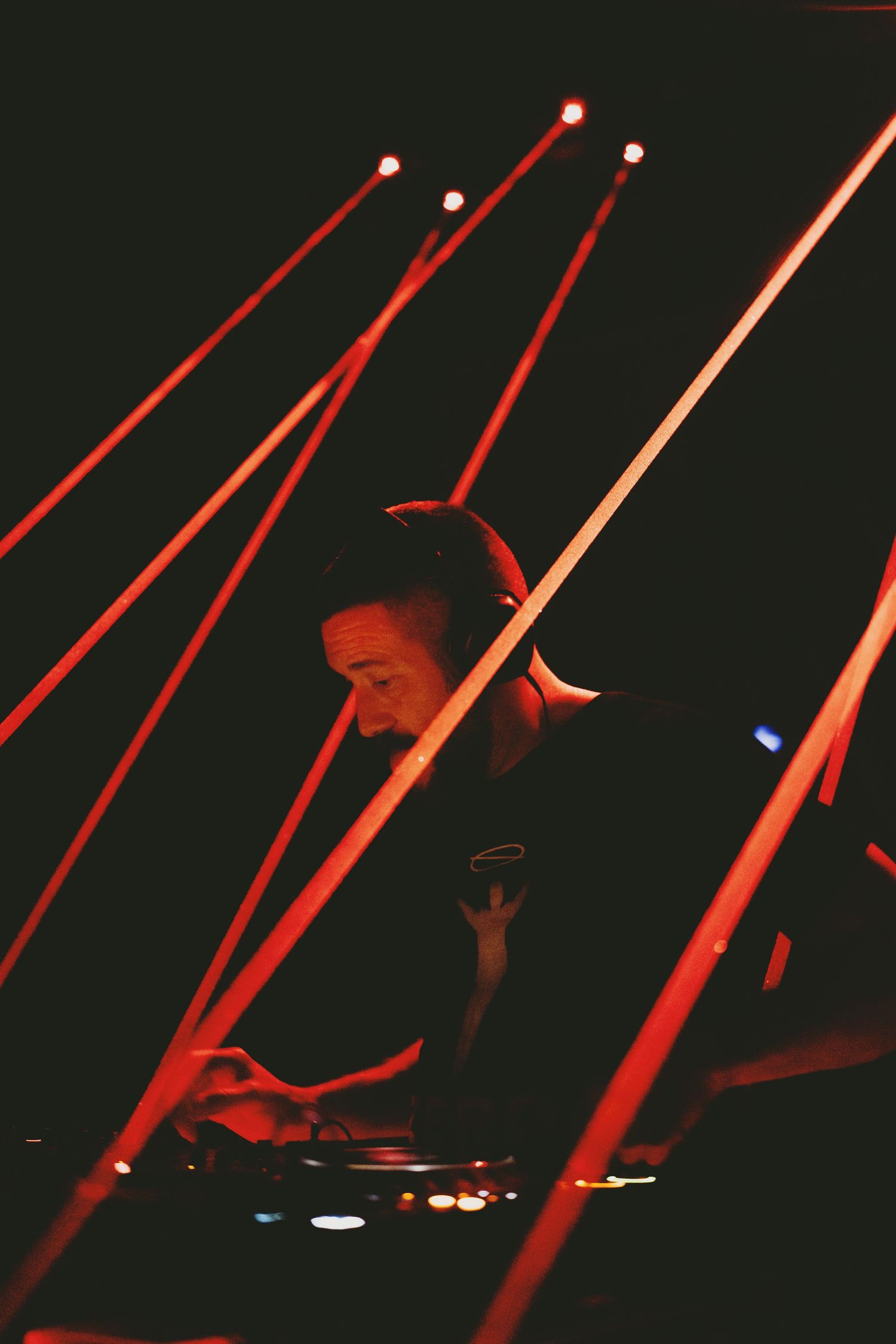 DJ performing at a dark concert venue surrounded by dramatic red laser lights beams.