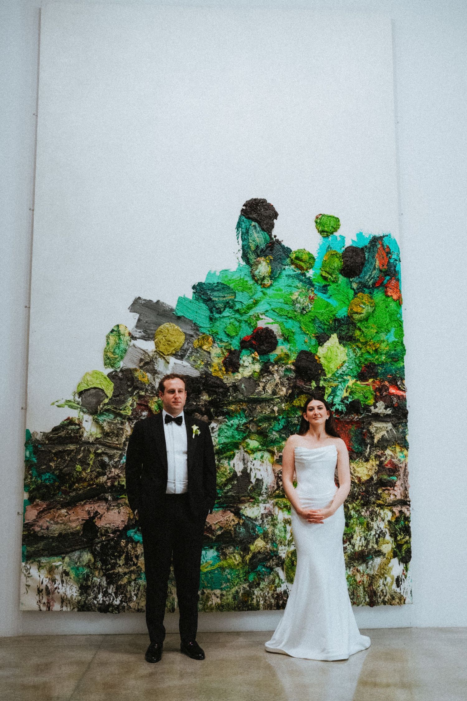 Bride and groom stand before a large colorful abstract painting in a white gallery during their wedding.