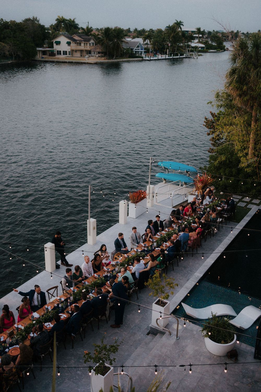Aerial view of a waterfront wedding reception with long tables on a dock.