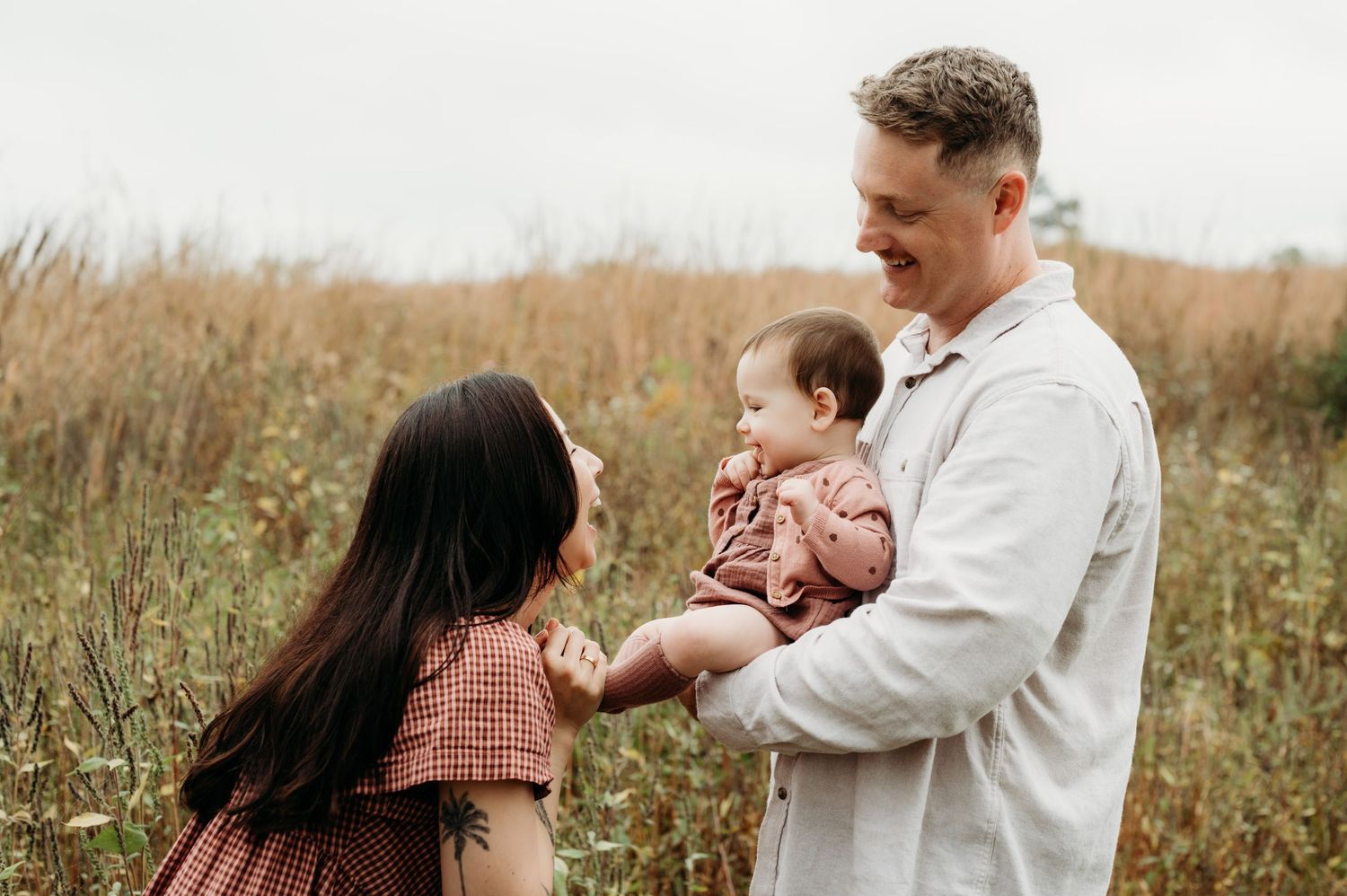 A family shares a tender moment together in a golden field of tall grass on an autumn day.