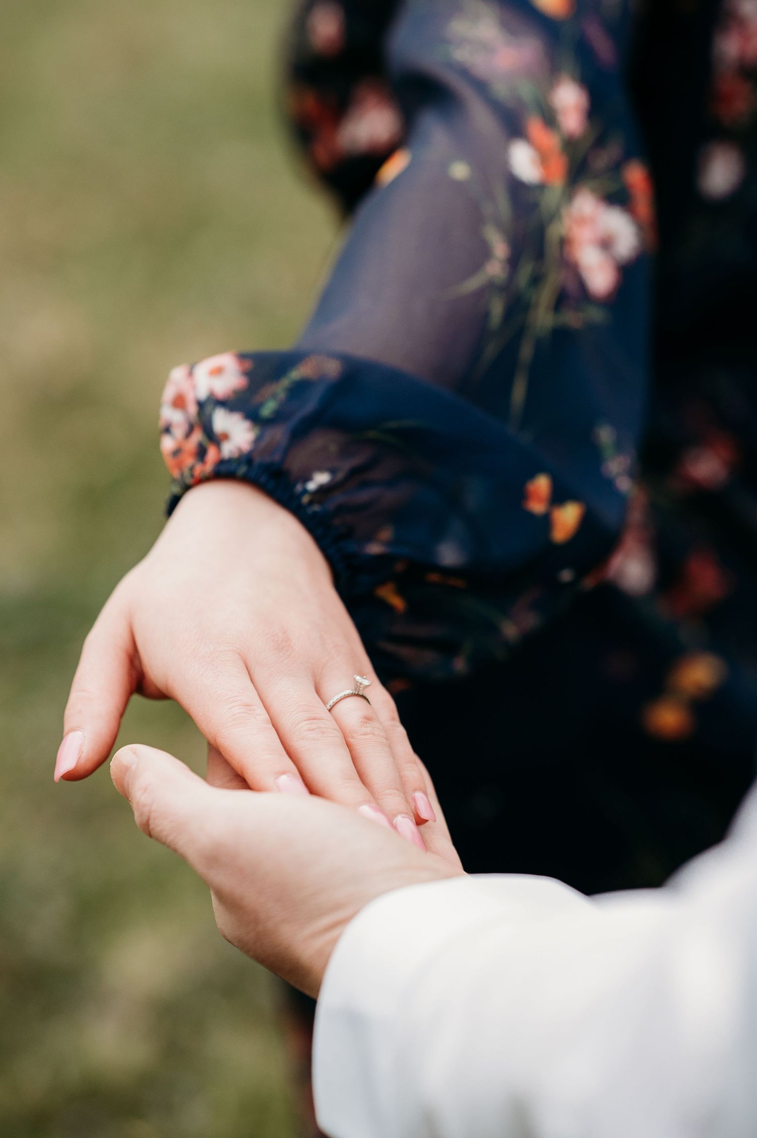 Gentle holding of hands outdoors with soft natural lighting and grass in background.