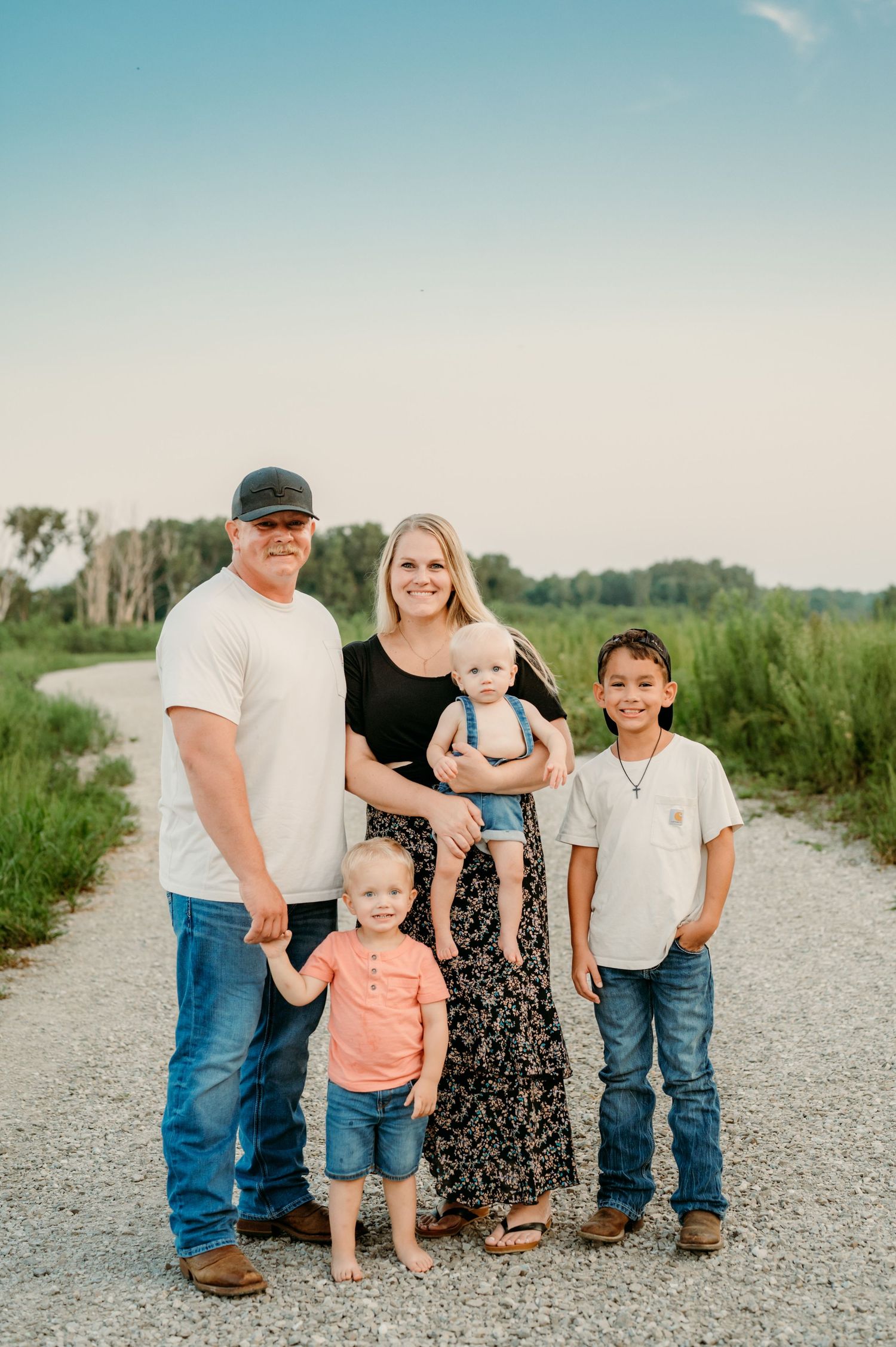 Family group portrait on a gravel path with natural scenery in the background at sunset.