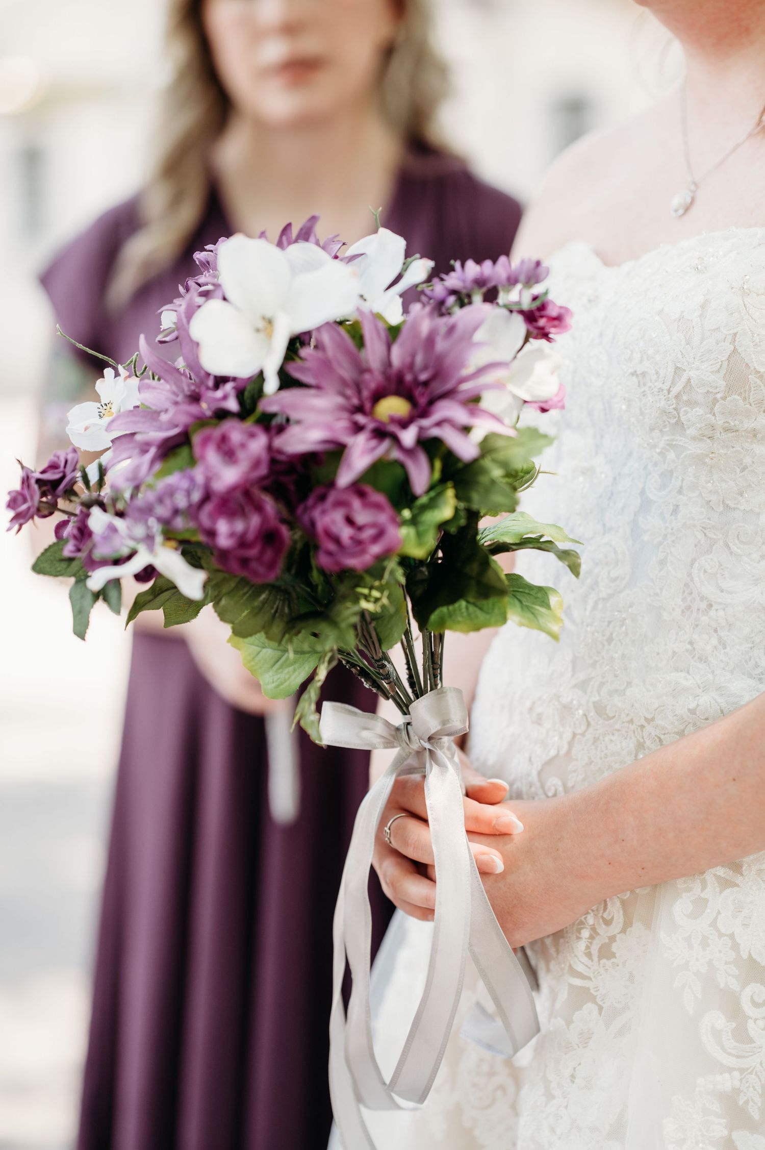 Purple and white wedding bouquets held against white lace dresses.