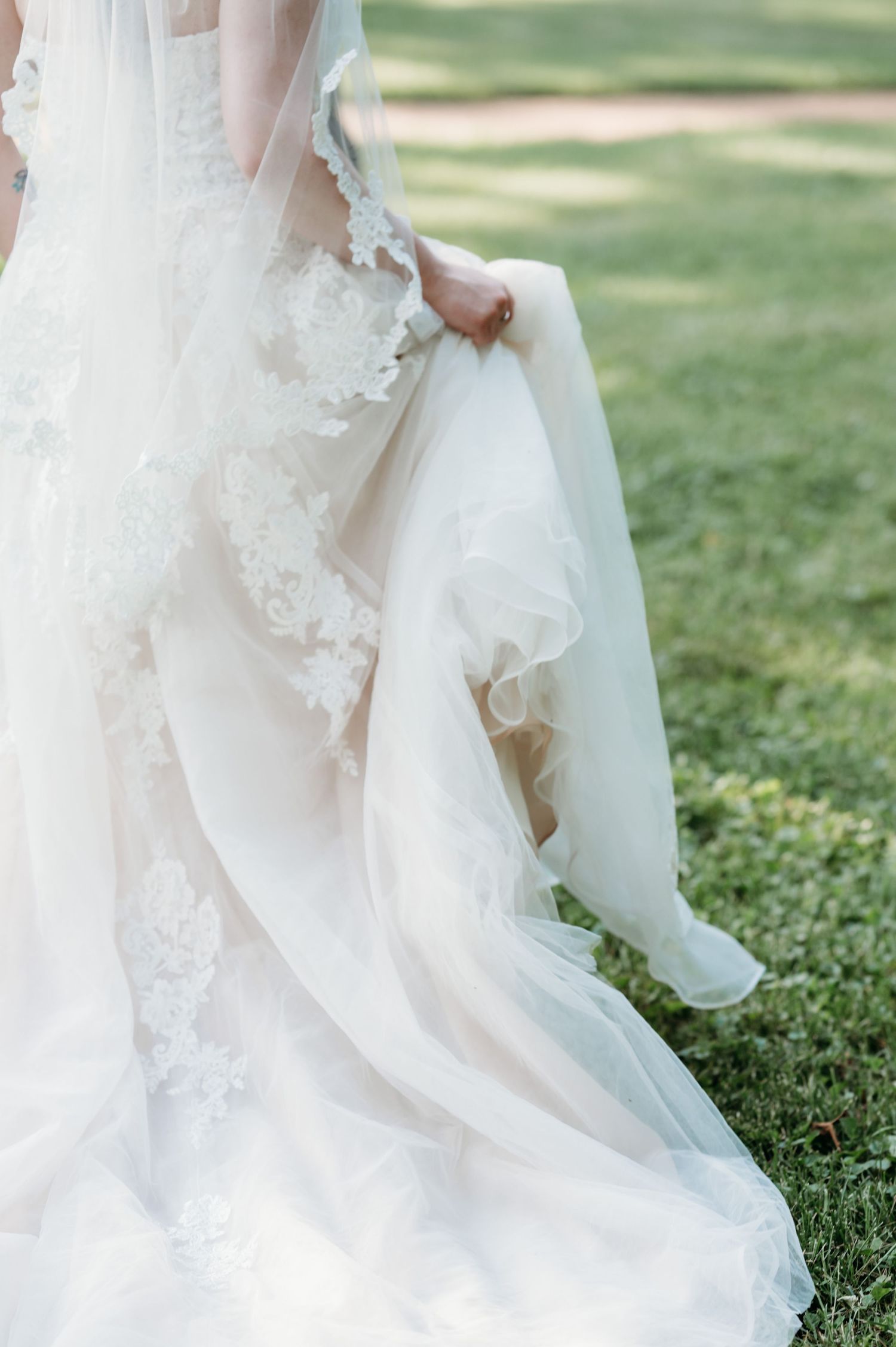 Details of a flowing white wedding dress with lace trim against green grass.