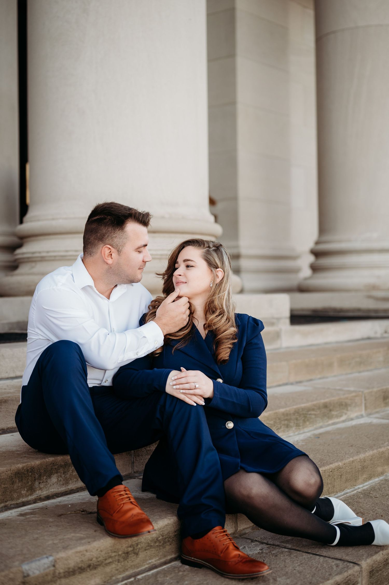 Couple sharing tender moment while sitting on stone steps near classical columns.