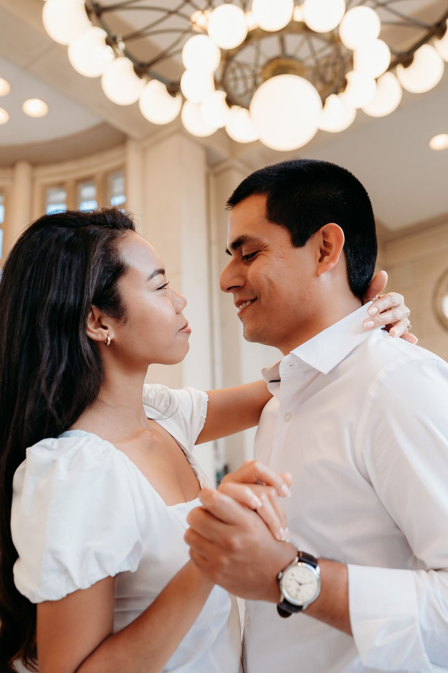 A couple dancing together under elegant glass globe lights indoors.