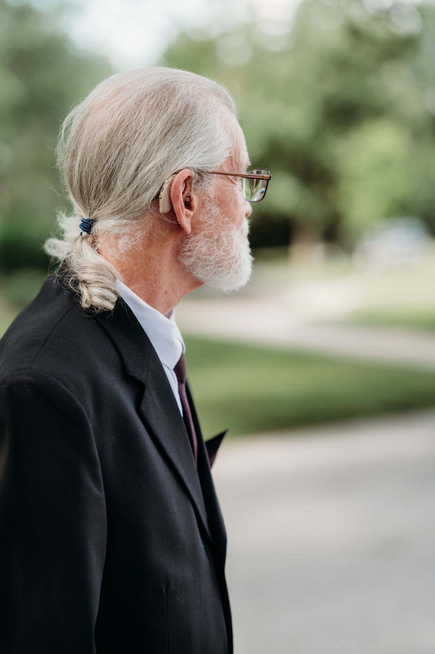 Profile views of an elderly person with white hair and glasses wearing a black suit.