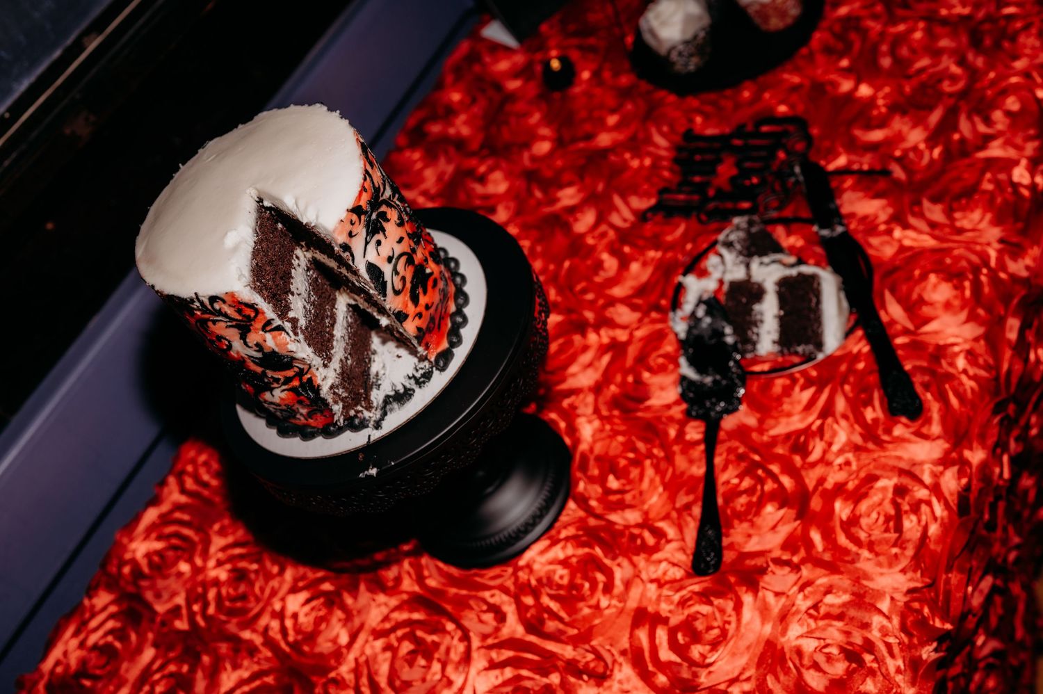 A chocolate dessert with whipped cream sits on a red floral tablecloth next to an ornate black candle holder.
