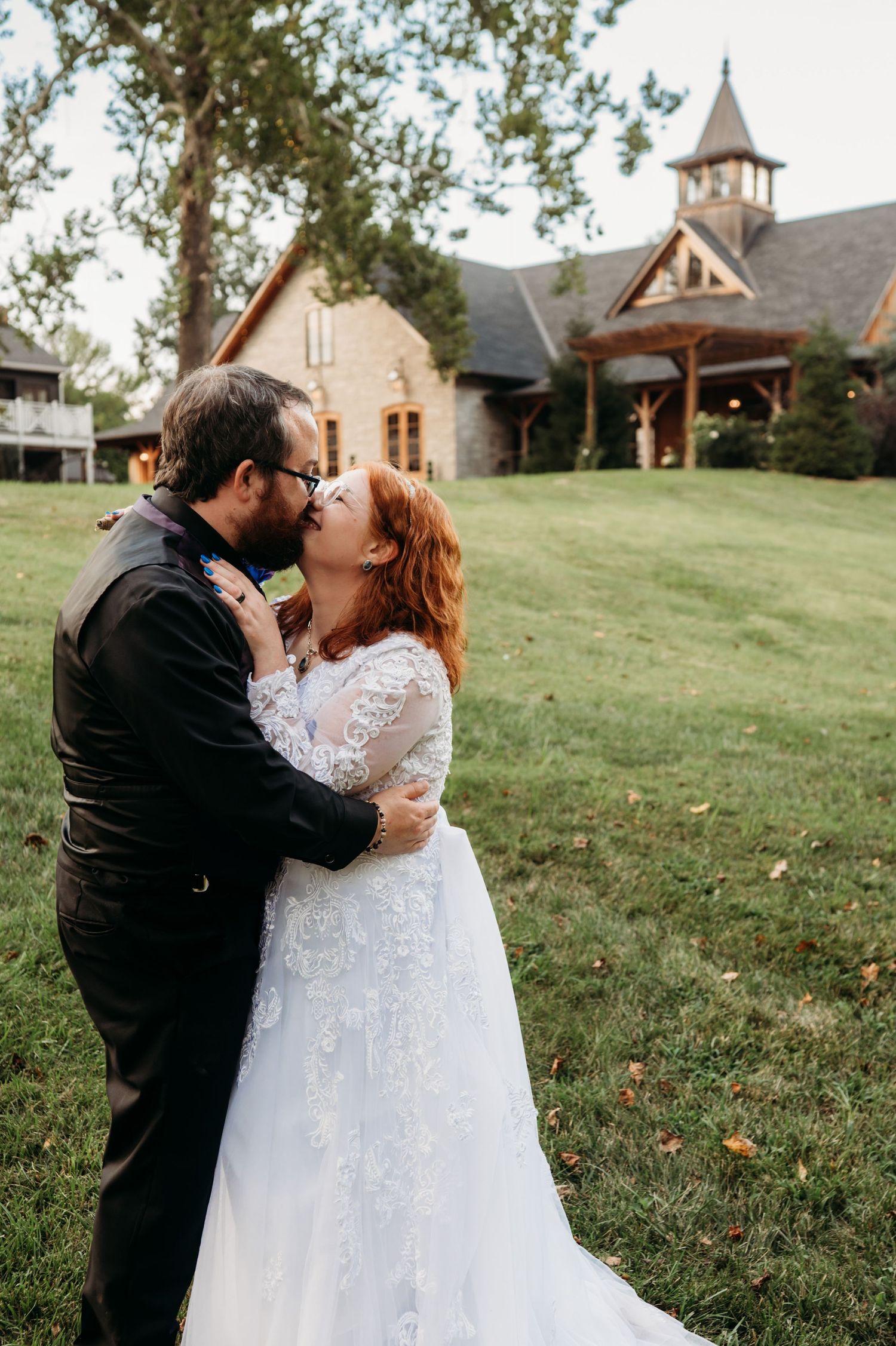 Romantic moment captured between newlyweds on a grassy hill with a church in the background.